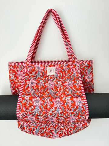 A red fabric tote bag with a pink and blue floral pattern, featuring red and white striped handles and trim, displayed against a white background.