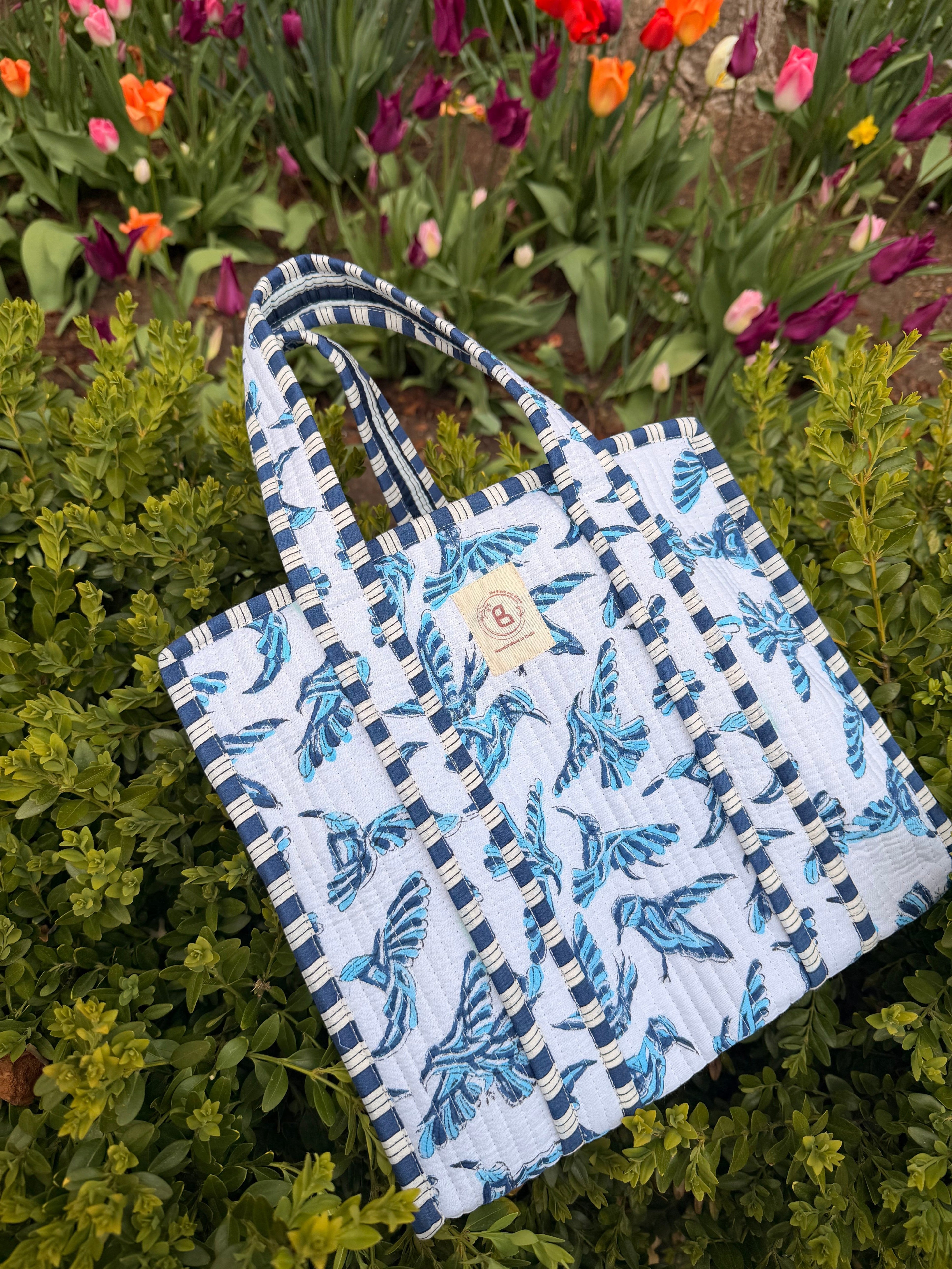 The Block & Bloom blue bird quilted mini tote with hand block-printed pattern, resting on green garden foliage.