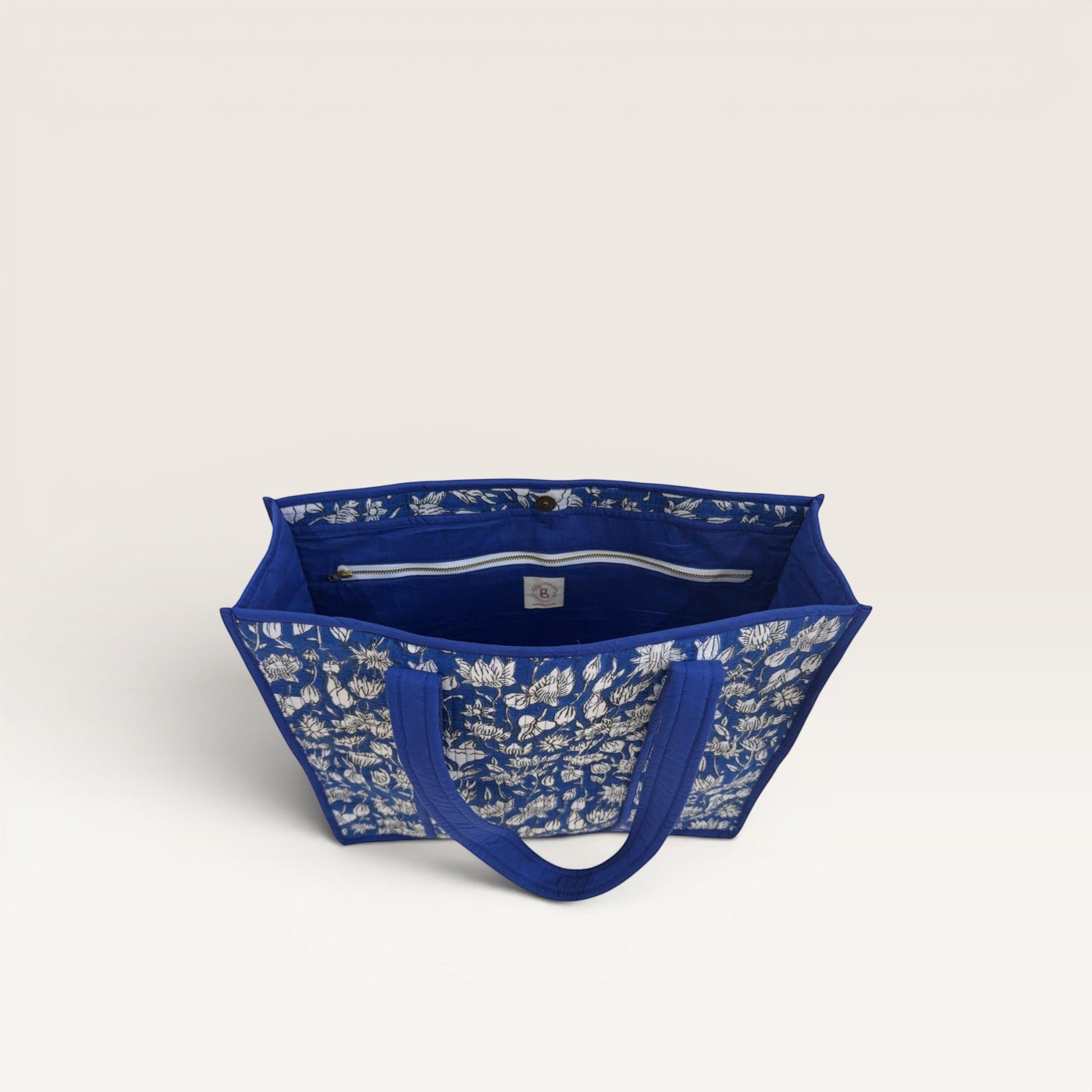 The Block & Bloom cobalt blue quilted tote bag with white lotus block print, featuring an open interior view.