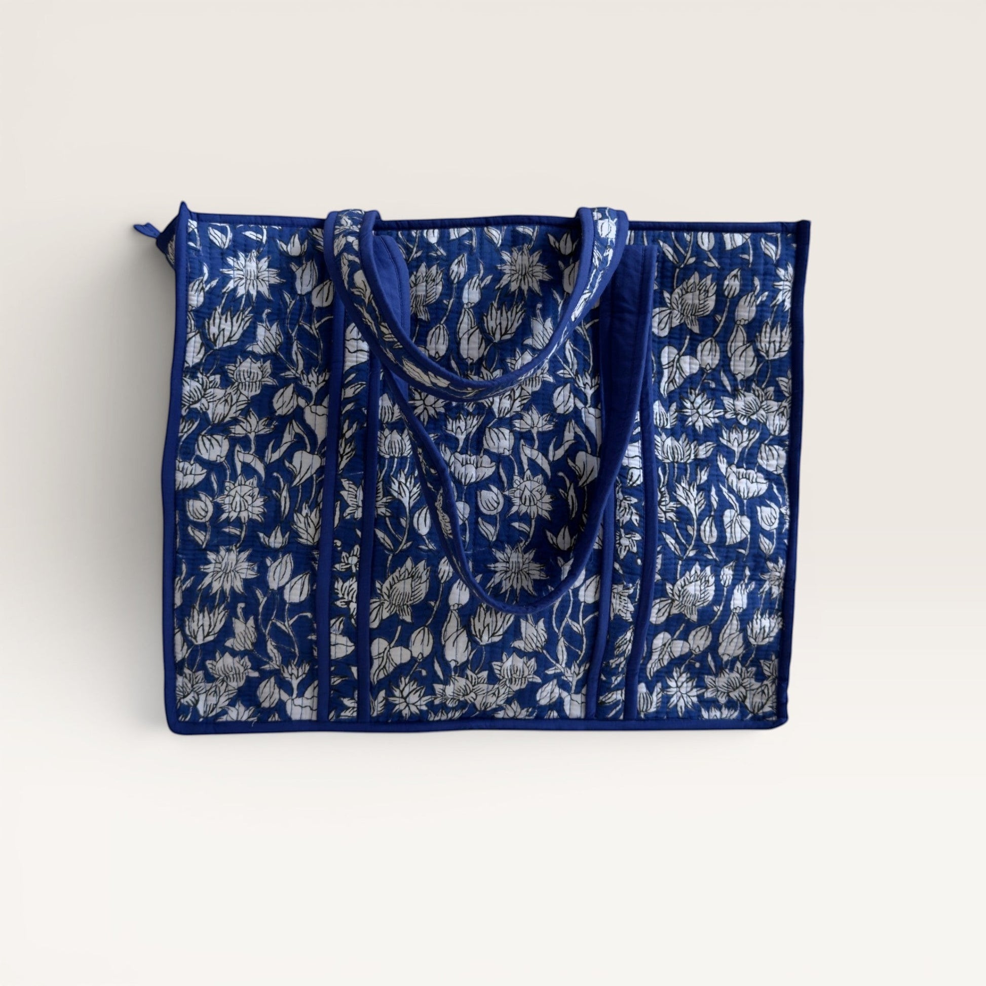 The Block & Bloom quilted tote bag in cobalt blue with a white hand-block printed lotus floral pattern.