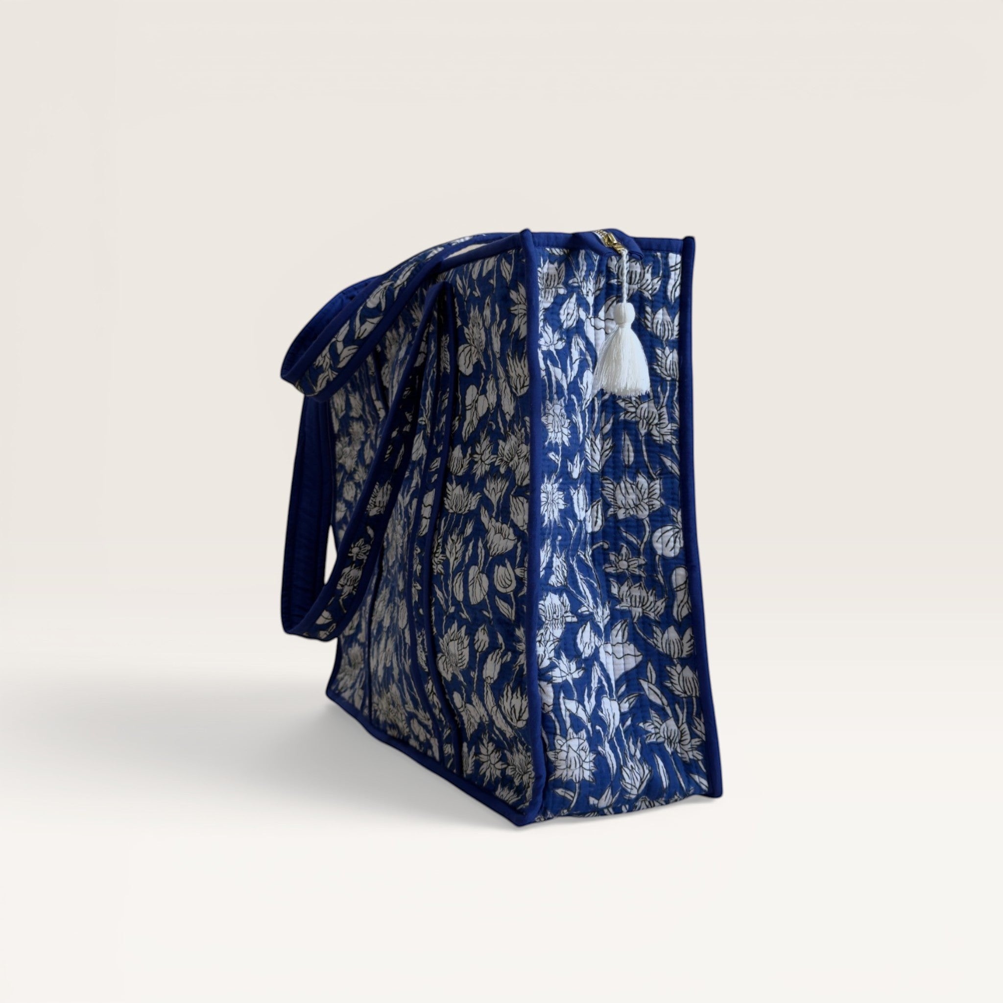 The Block & Bloom cobalt blue quilted tote bag with white hand block printed lotus flowers and a side tassel detail.
