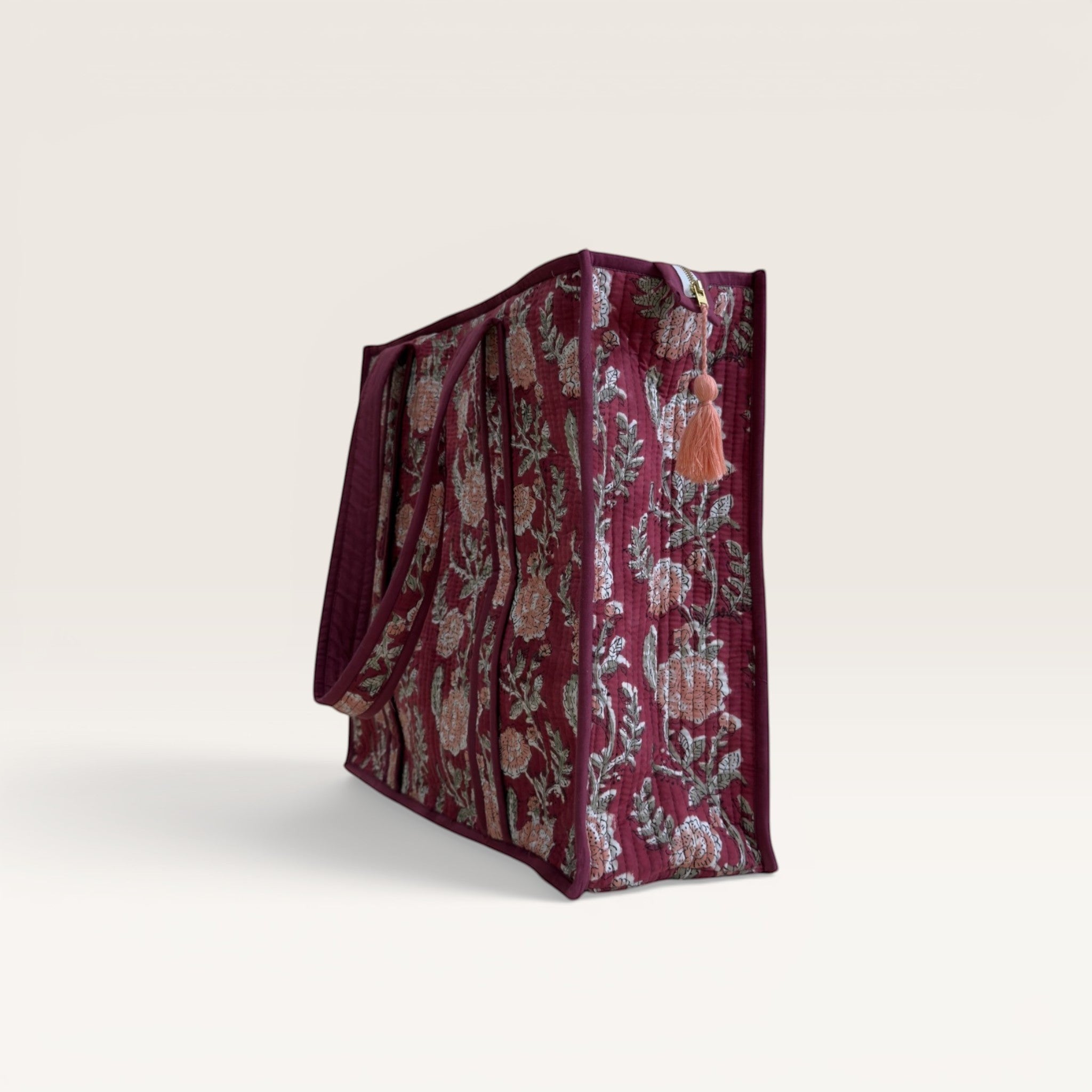 The Block & Bloom burgundy quilted tote bag with pink rose floral print and side tassel detail.