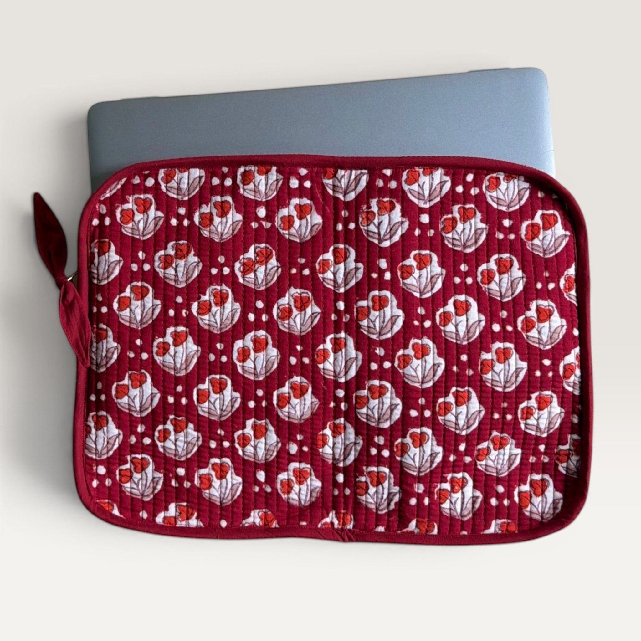 The Block & Bloom quilted laptop sleeve in burgundy red with red tulip motifs, white dots, and a fabric bow zipper.