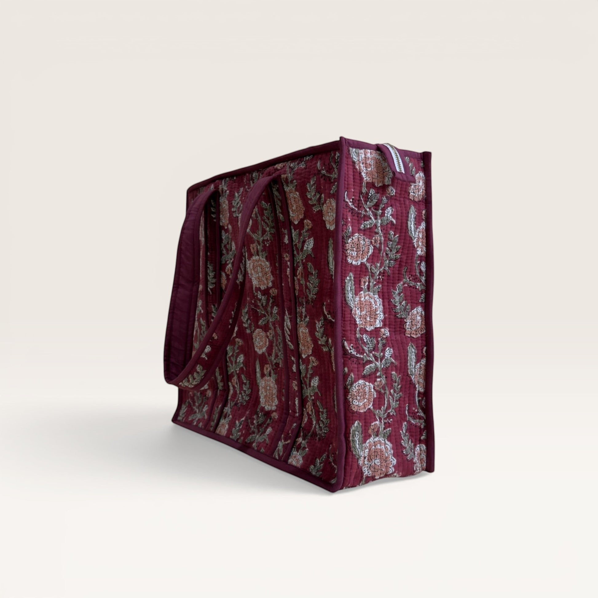 The Block & Bloom quilted tote in burgundy with a pink rose and green foliage hand block print, side view.