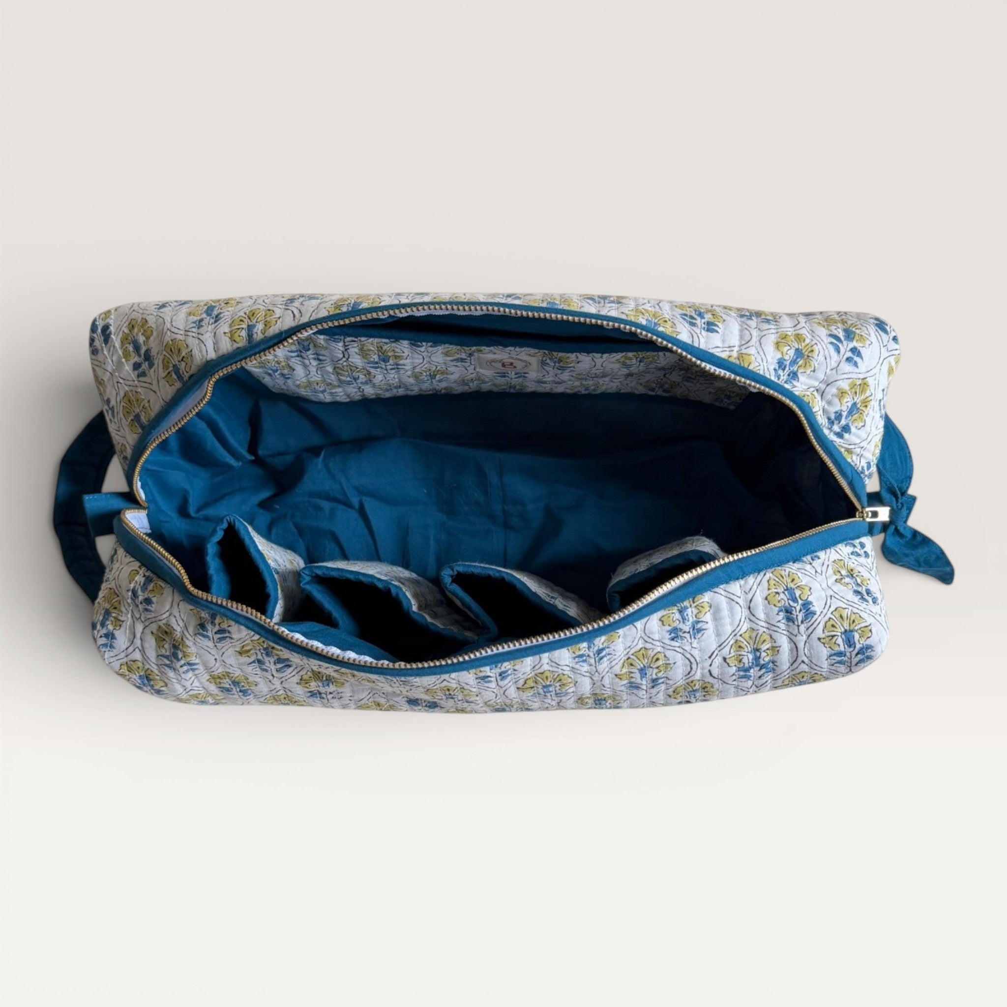 The Block & Bloom Cosmos Tile quilted hair tool organizer bag with blue and yellow floral print and interior slots.