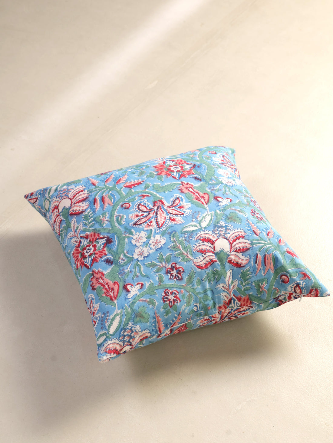 The Block & Bloom hand block printed cotton cushion cover featuring red, rose, and white floral patterns on blue.