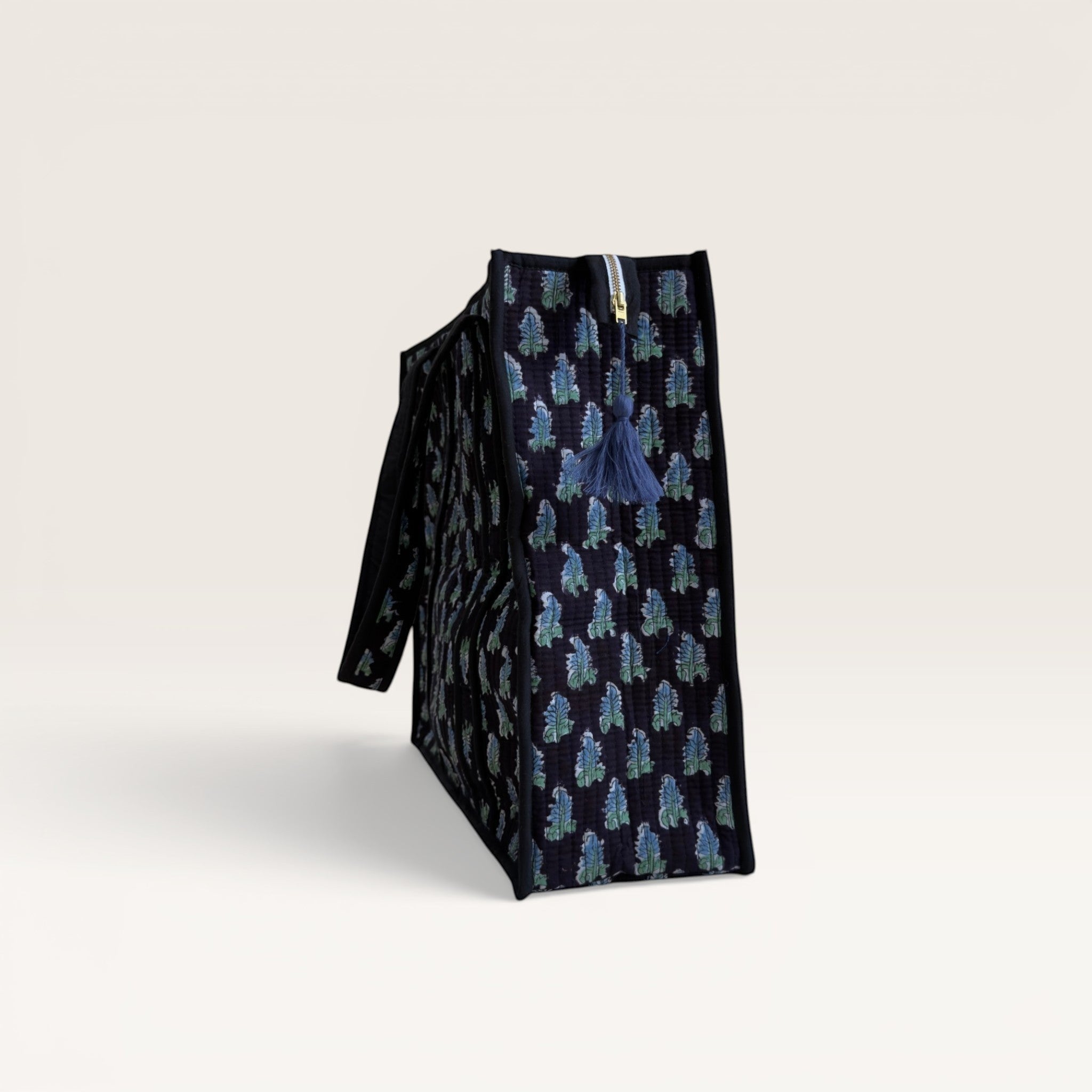 The Block & Bloom Midnight Fern quilted tote bag in black with blue and sage green leaf print and side tassel detail.