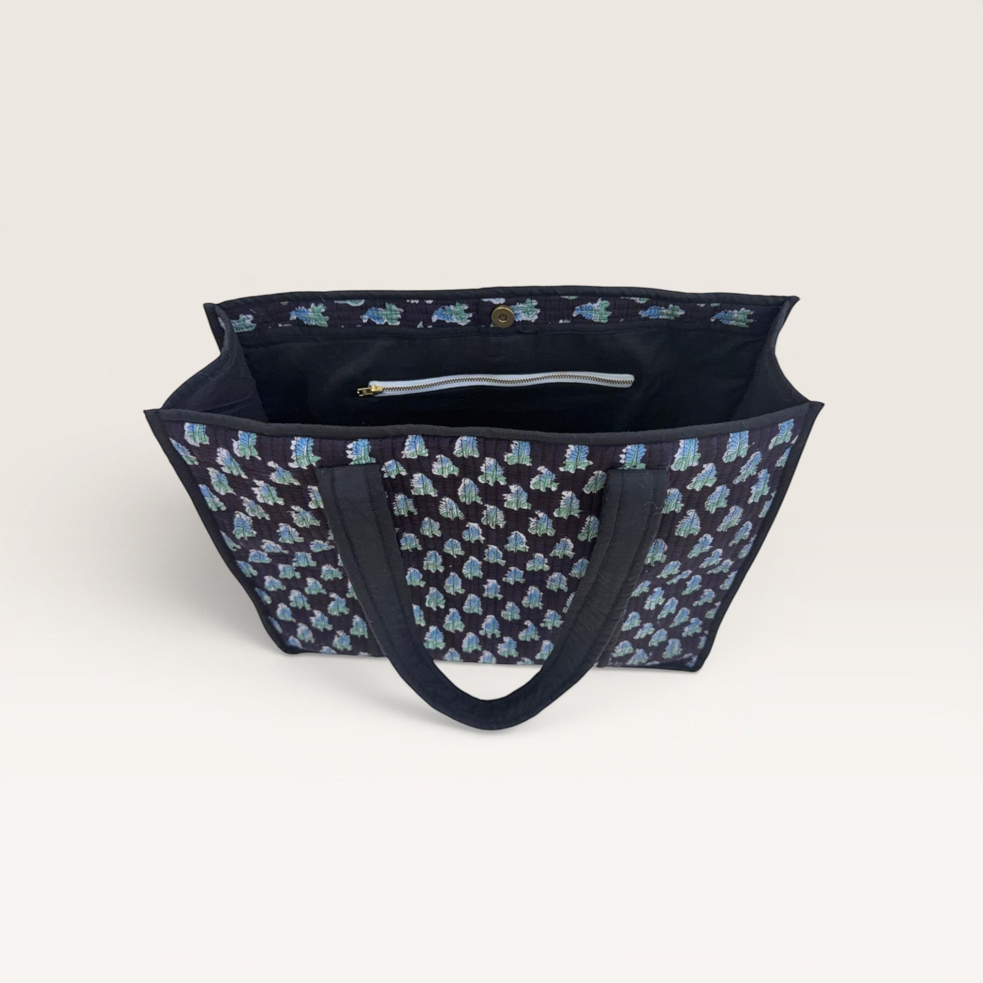 The Block & Bloom Midnight Fern quilted tote bag in black with blue and sage green leaf print and interior pockets.