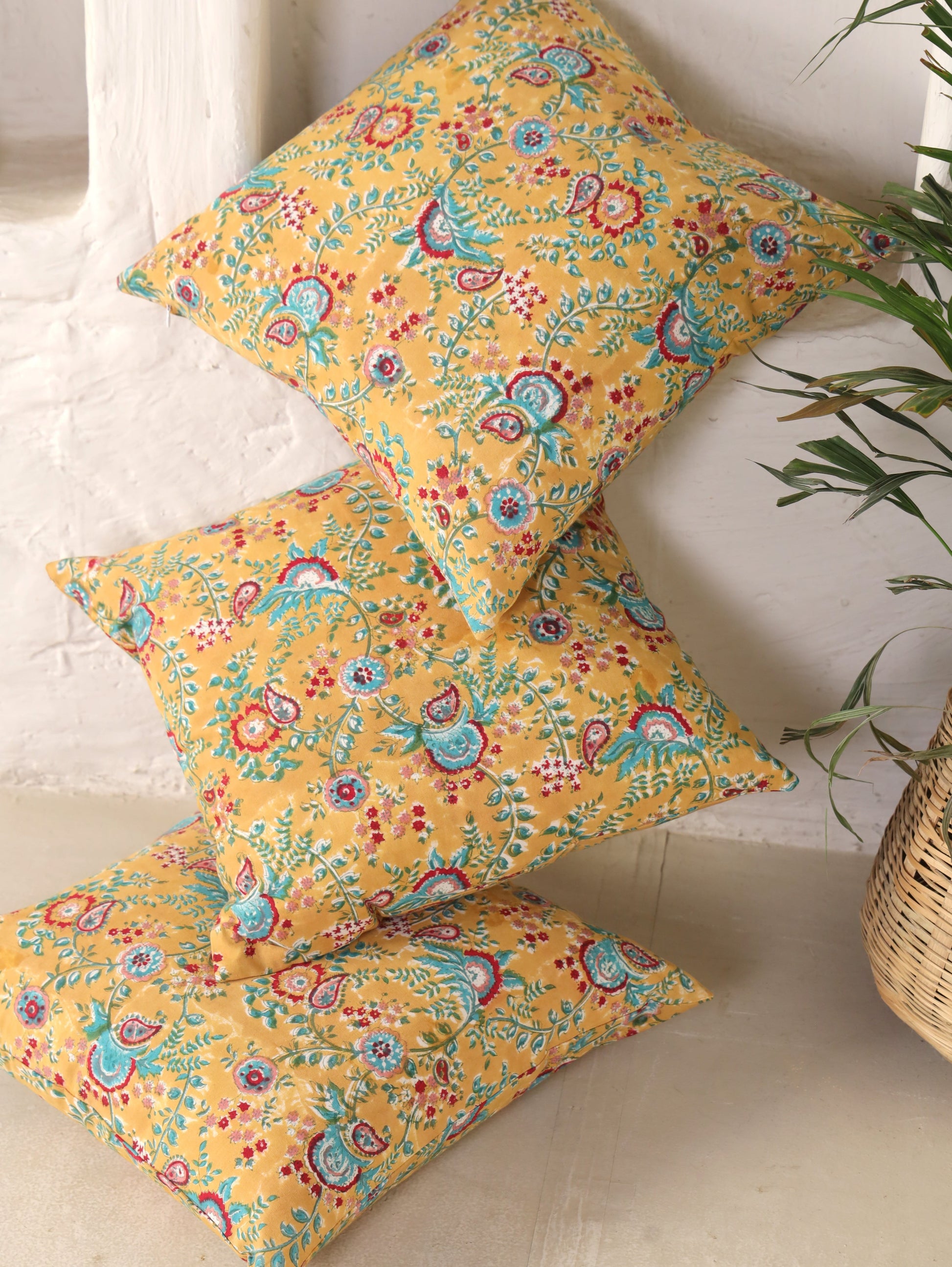 The Block & Bloom mustard cotton cushion covers featuring hand-block printed teal and crimson paisley floral patterns.
