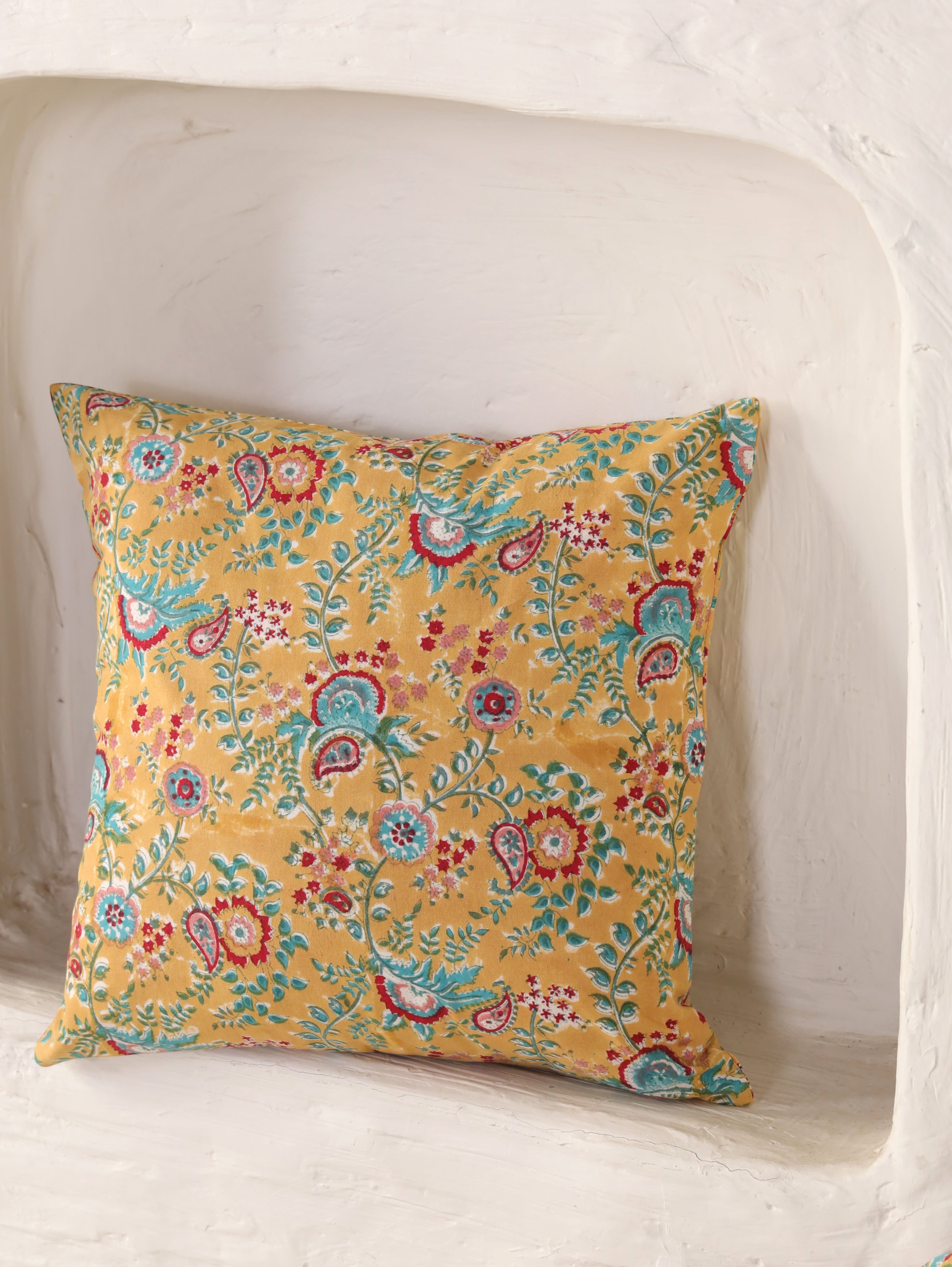 The Block & Bloom mustard cotton cushion cover featuring hand block printed teal and crimson paisley floral patterns.