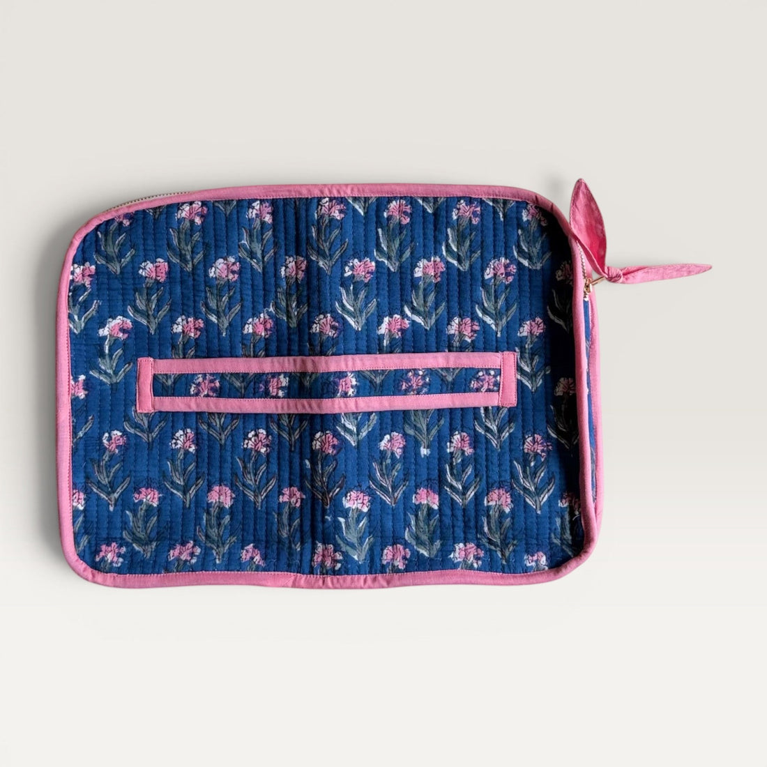The Block & Bloom navy blue quilted laptop sleeve with pink carnation floral print and a pink fabric bow zipper pull.