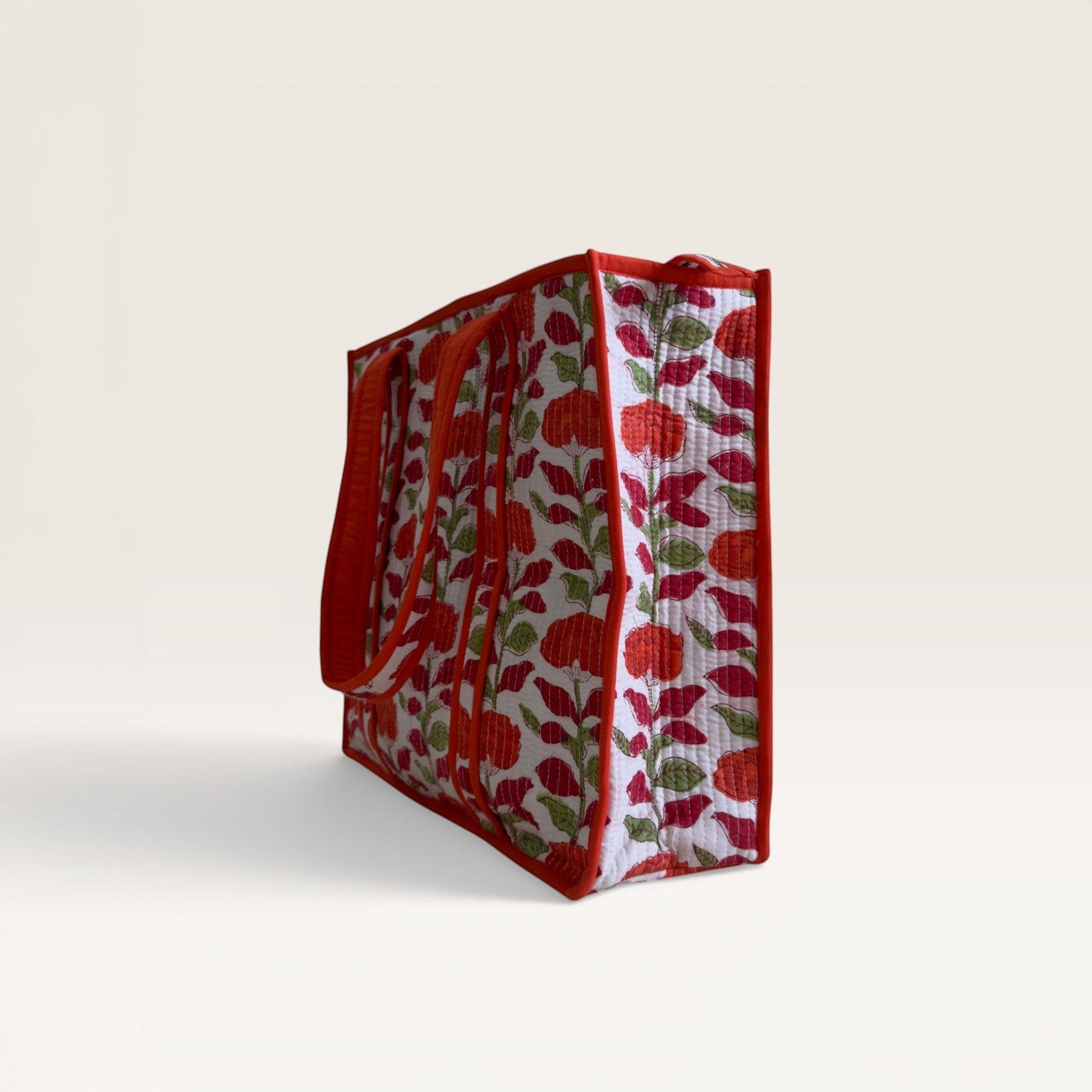 The Block & Bloom quilted tote bag in white with orange carnation floral print and red trim, side profile view.