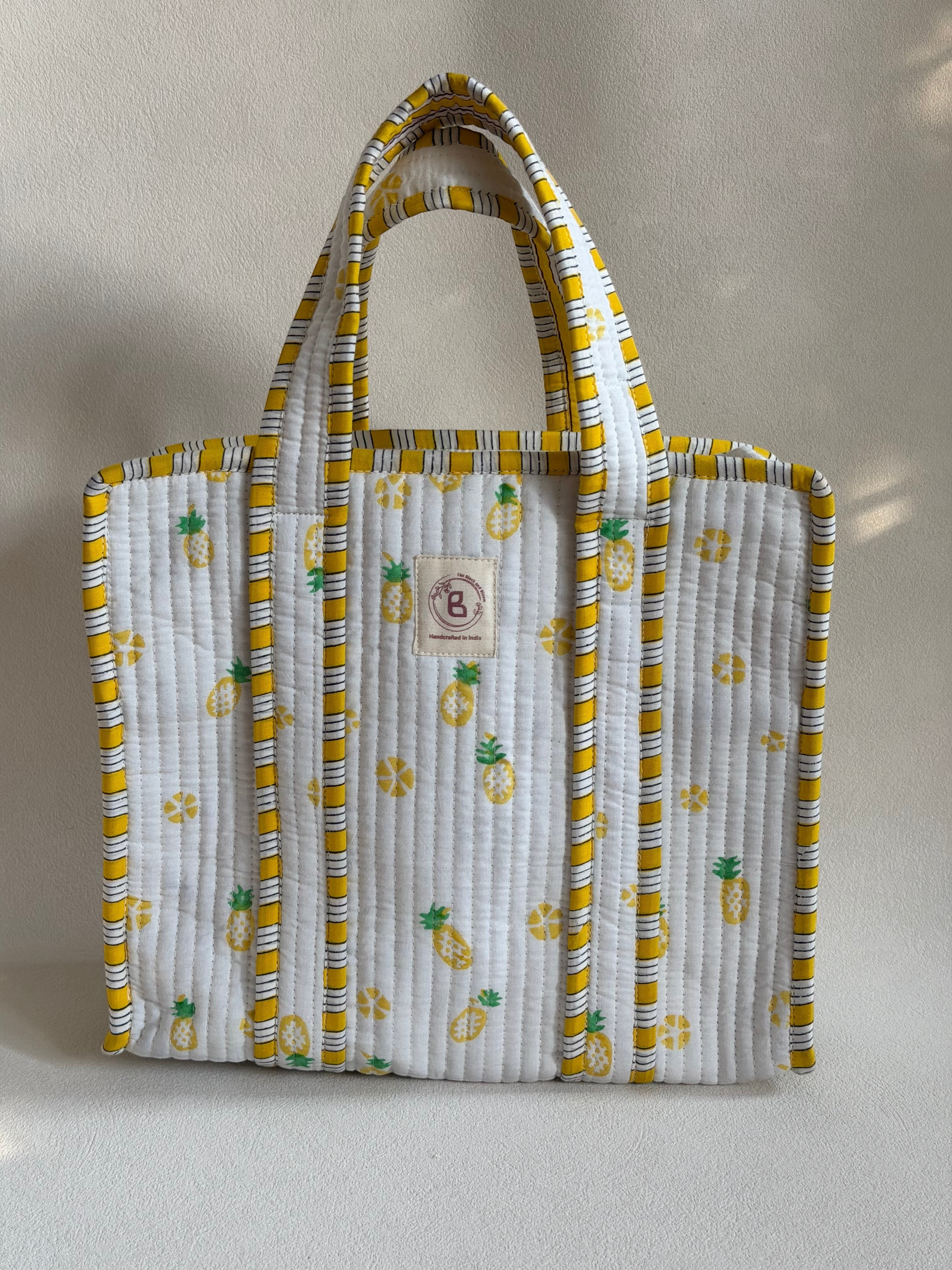 The Block & Bloom quilted mini tote in white with yellow and green pineapple print and striped trim.