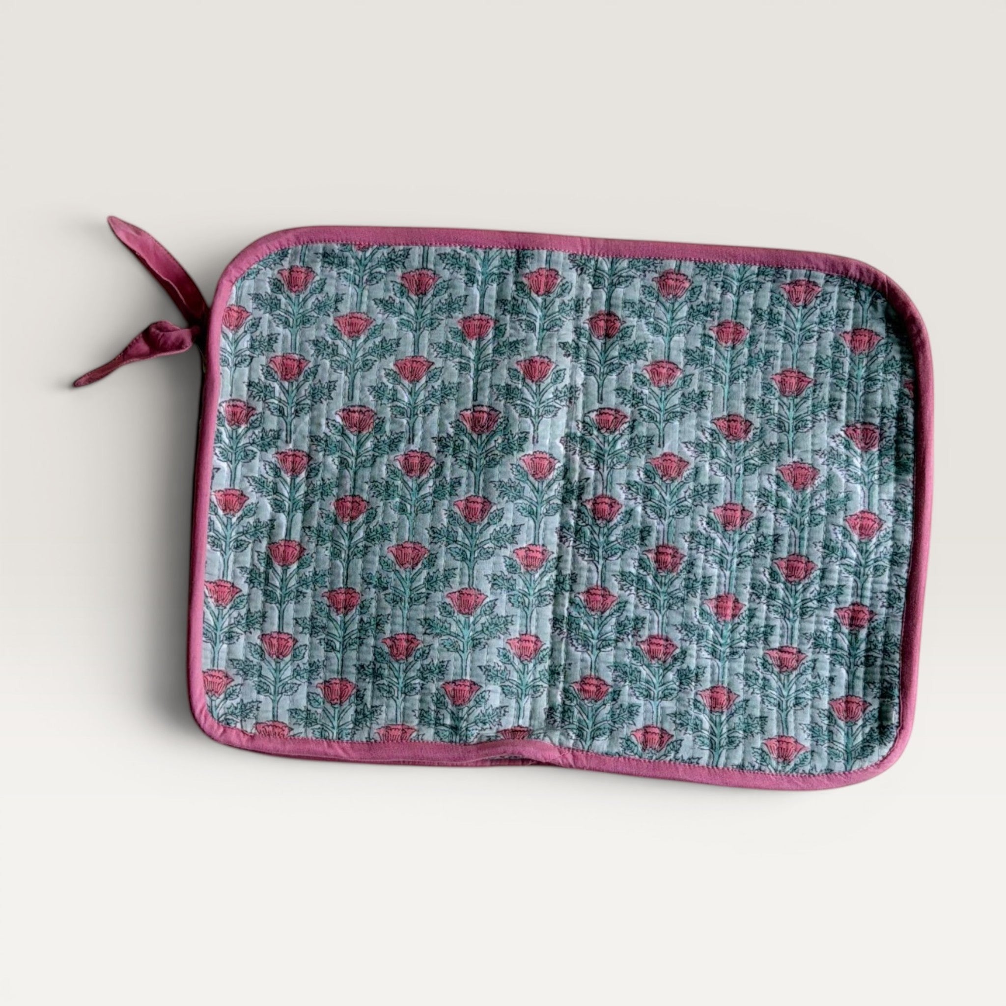 The Block & Bloom quilted laptop sleeve in sage green with a pink floral vine print and a fabric bow zipper pull.