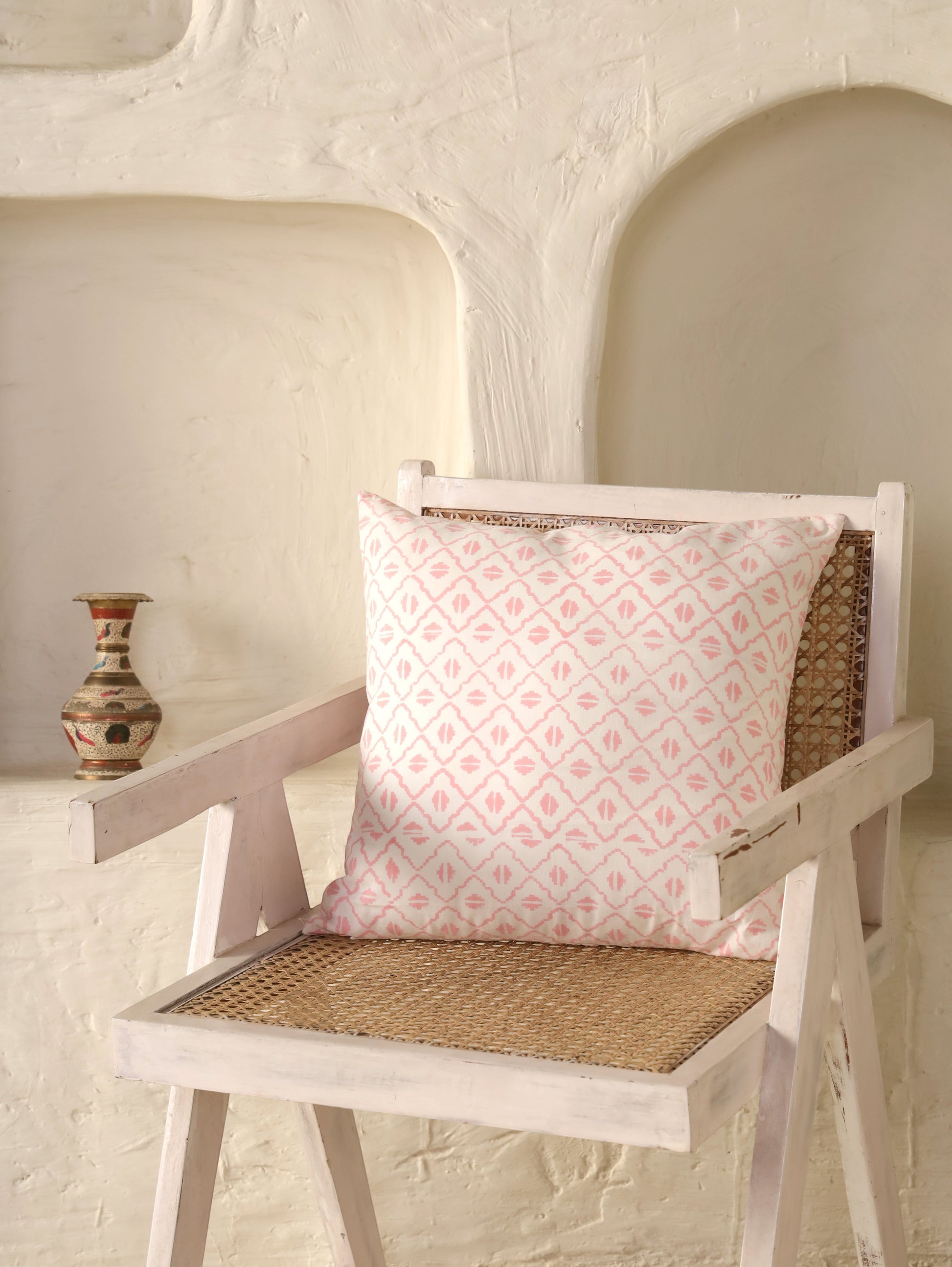 The Block & Bloom pink and ivory cotton cushion cover with a hand-blocked geometric diamond lattice pattern on a chair