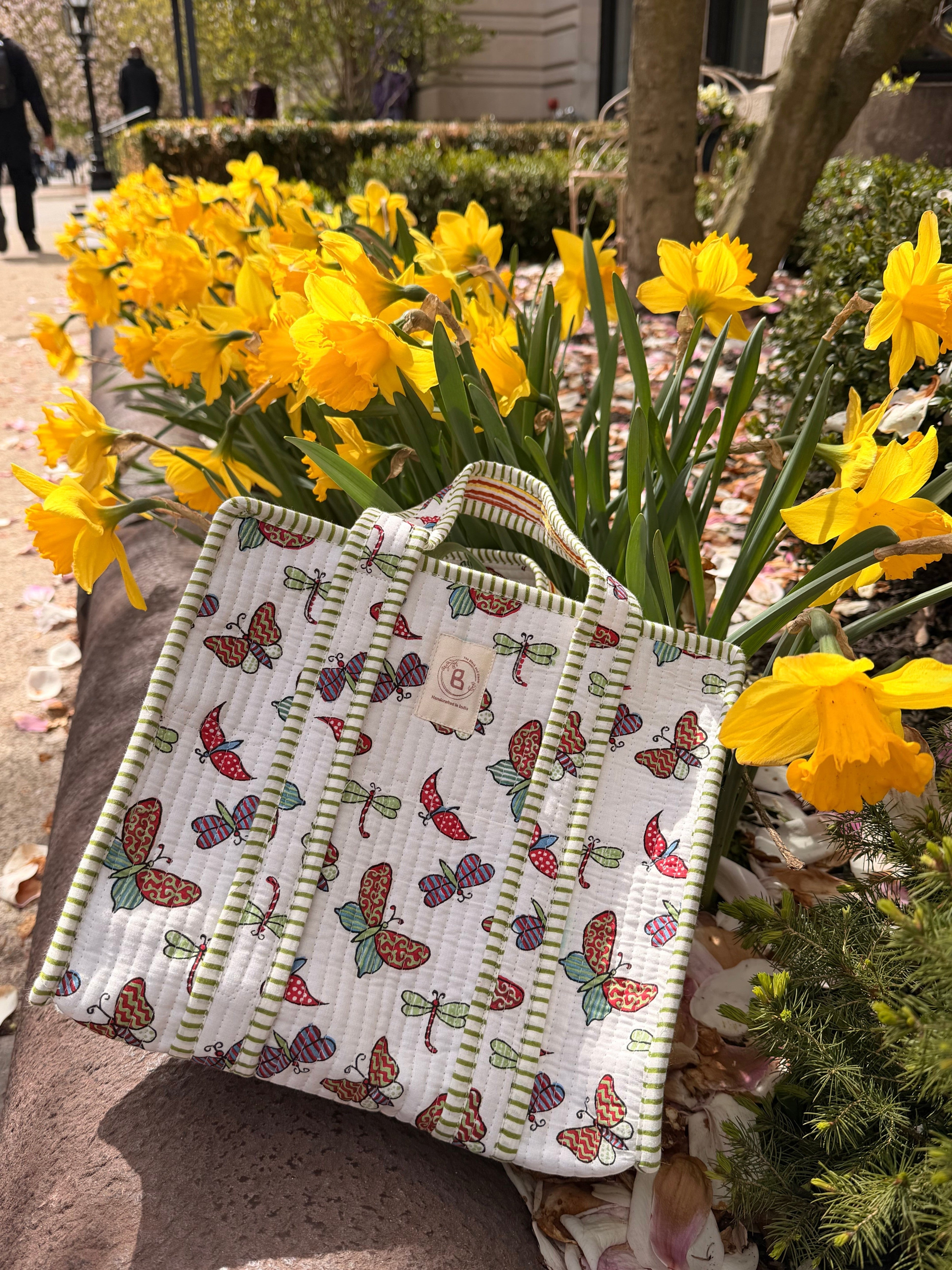 The Block & Bloom quilted mini tote with butterfly and dragonfly print, green striped trim, set among yellow flowers.