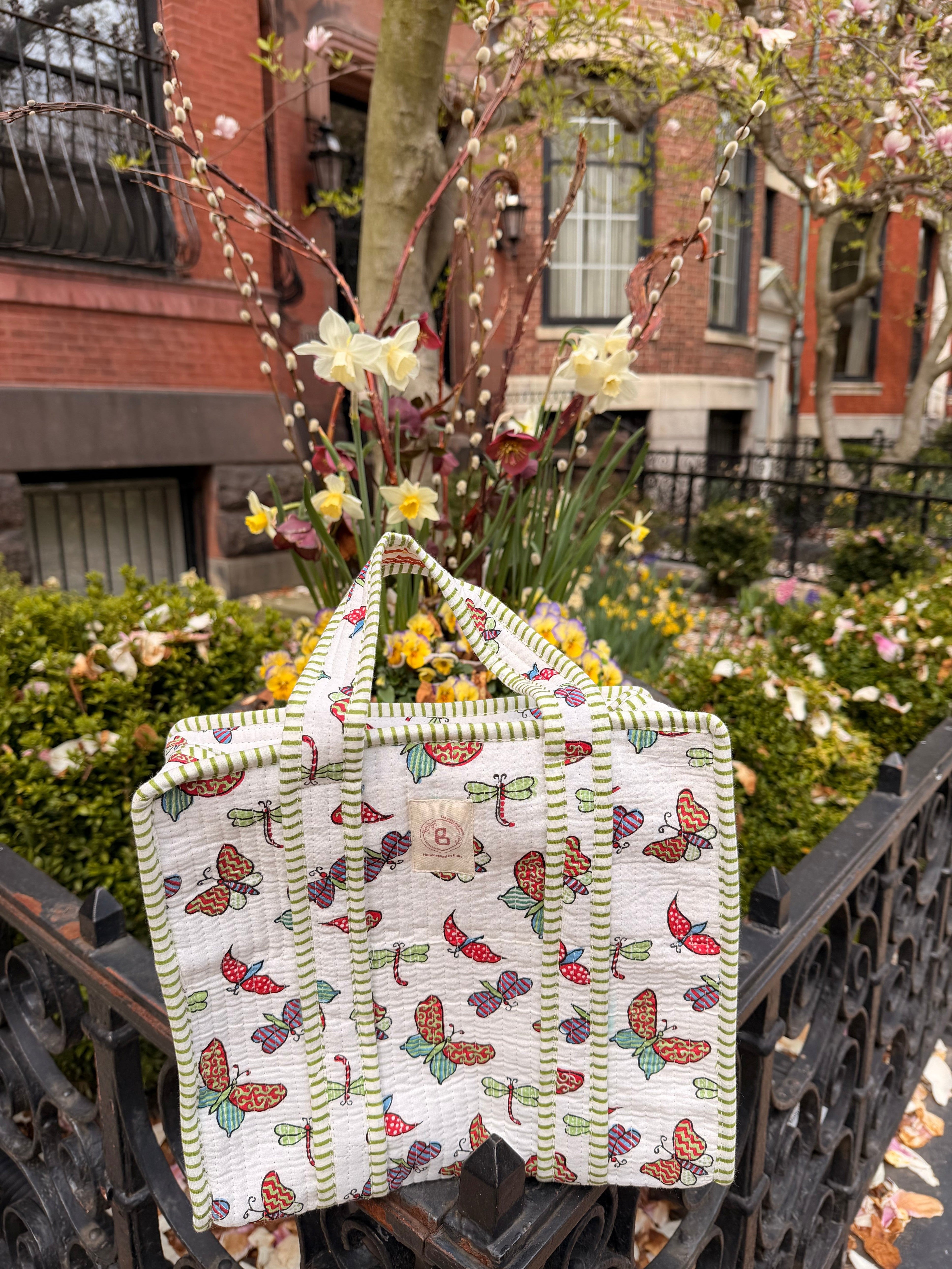 The Block & Bloom butterfly and dragonfly print quilted mini tote bag with green striped trim in a garden setting.