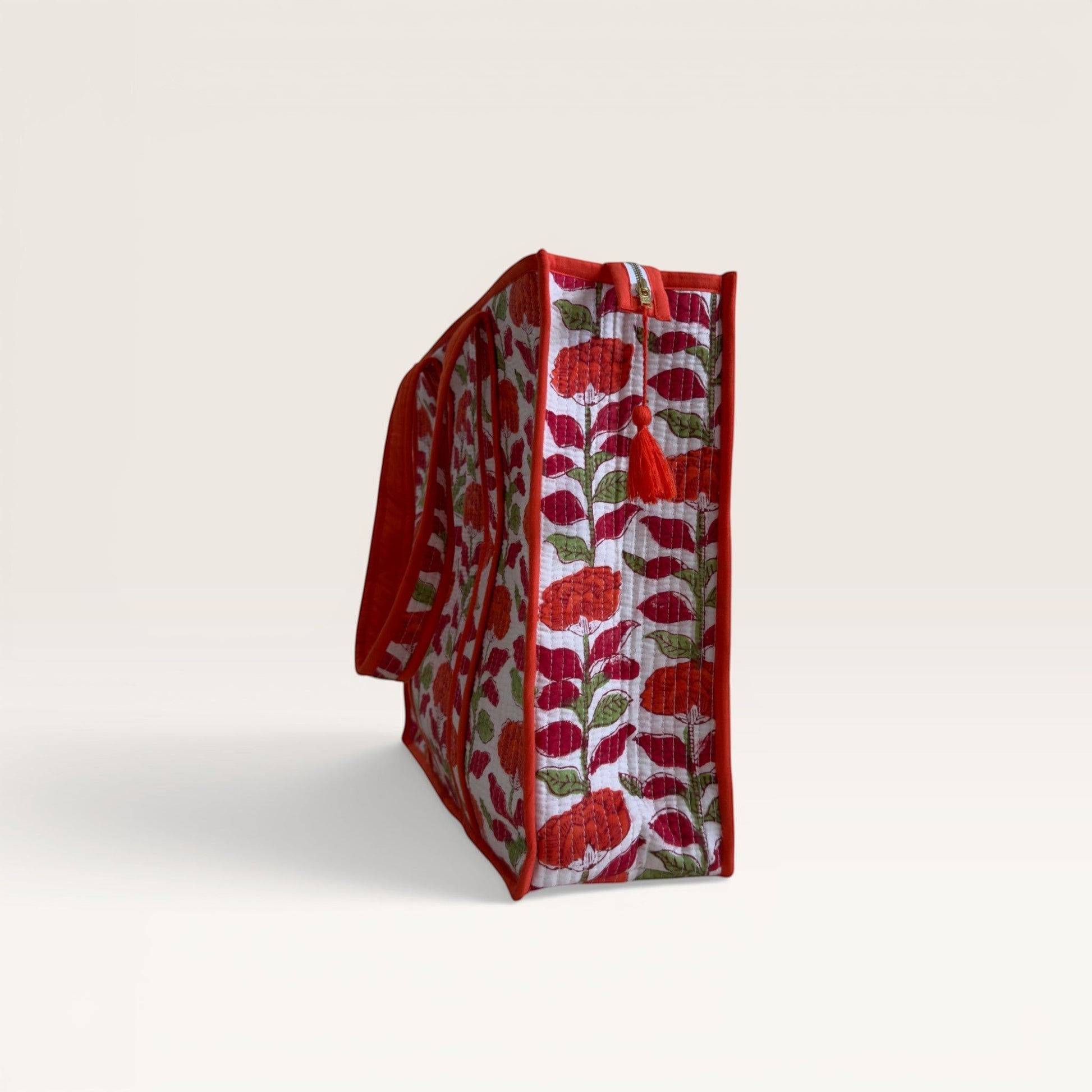 The Block & Bloom quilted tote bag in white with orange carnation floral print, red trim, and side tassel detail.