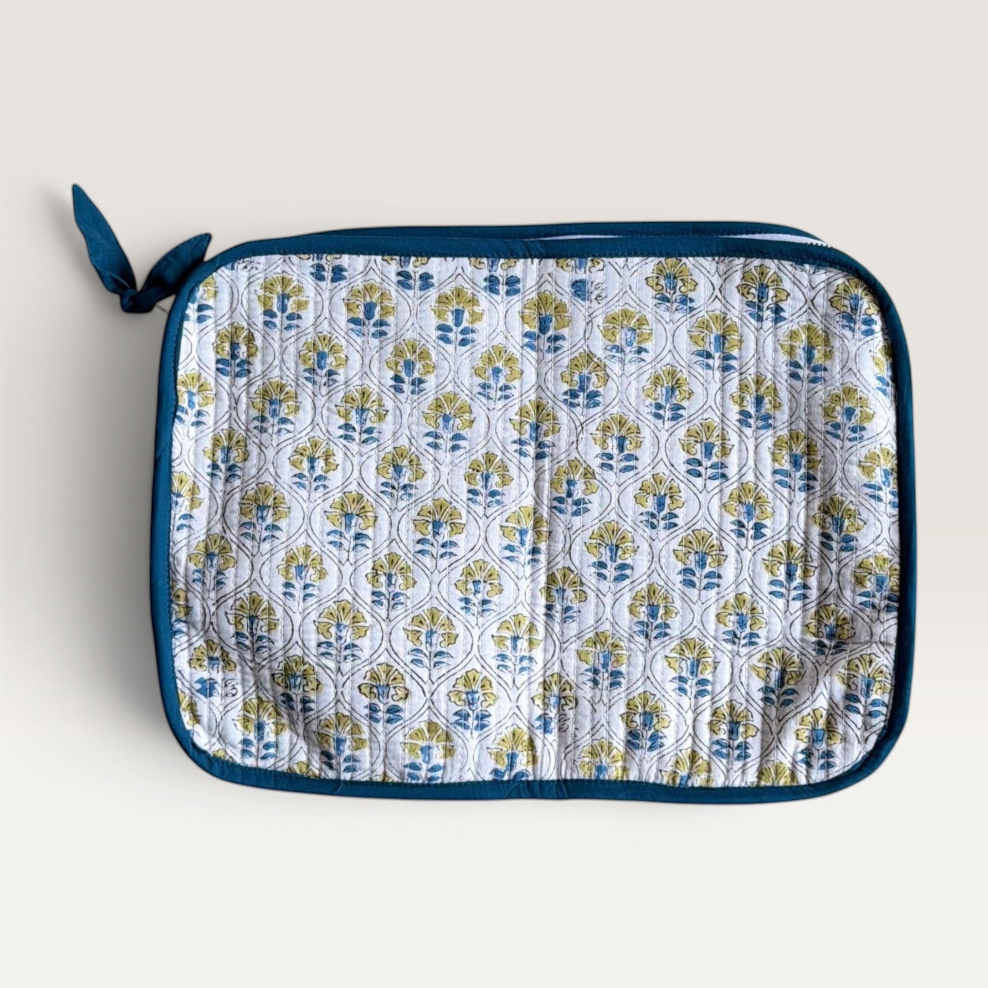 The Block & Bloom quilted laptop sleeve featuring a white, blue, and yellow floral tile pattern with a fabric bow zipper.