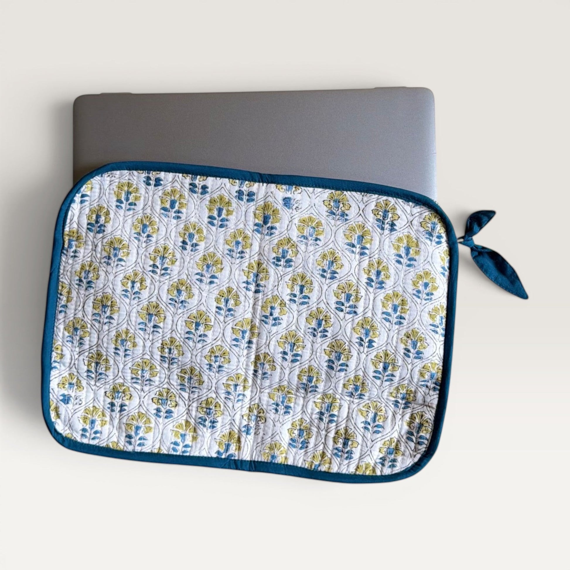 The Block & Bloom quilted laptop sleeve featuring a blue and yellow floral tile pattern on white with a fabric bow.