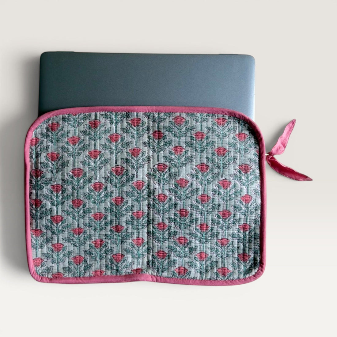 The Block & Bloom quilted laptop sleeve in sage green with pink floral vine print and a fabric bow zipper pull.