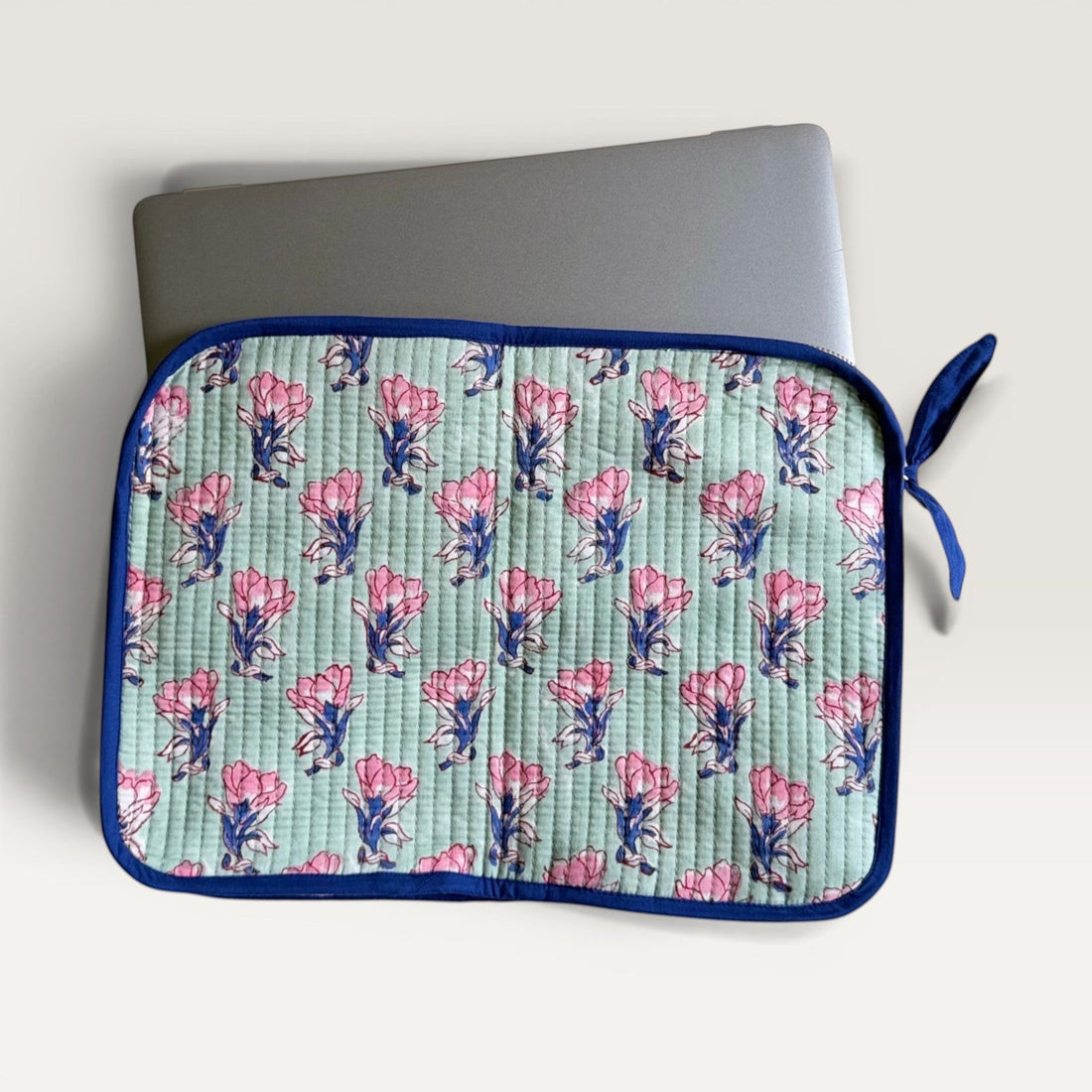 The Block & Bloom quilted laptop sleeve in sage green with pink saffron flower print and navy blue trim.