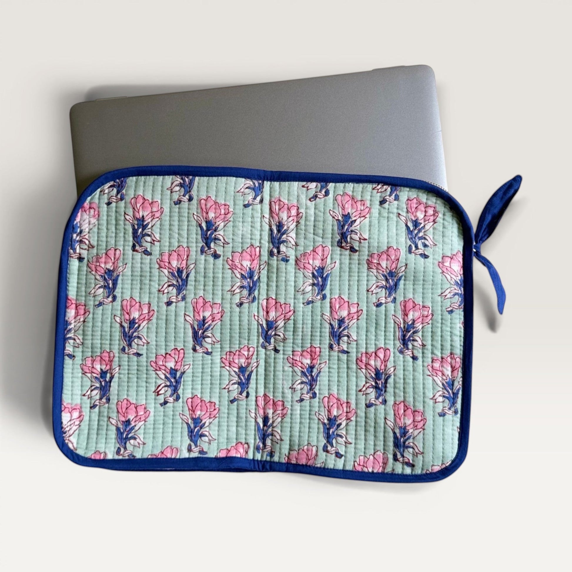 The Block & Bloom quilted laptop sleeve in sage green with pink saffron flower print and navy blue trim.
