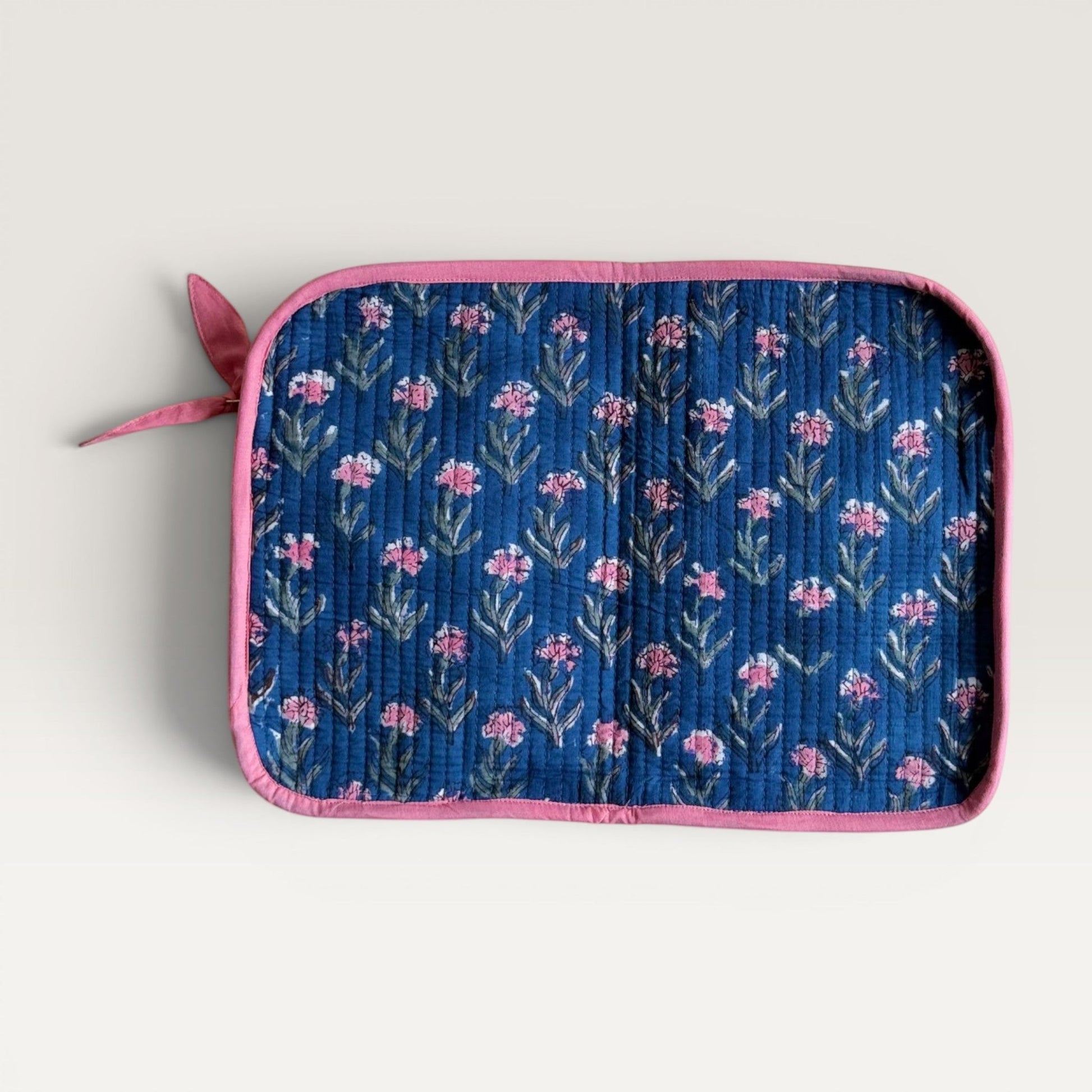 The Block & Bloom quilted navy blue laptop sleeve with pink carnation floral print and a decorative fabric bow zipper.