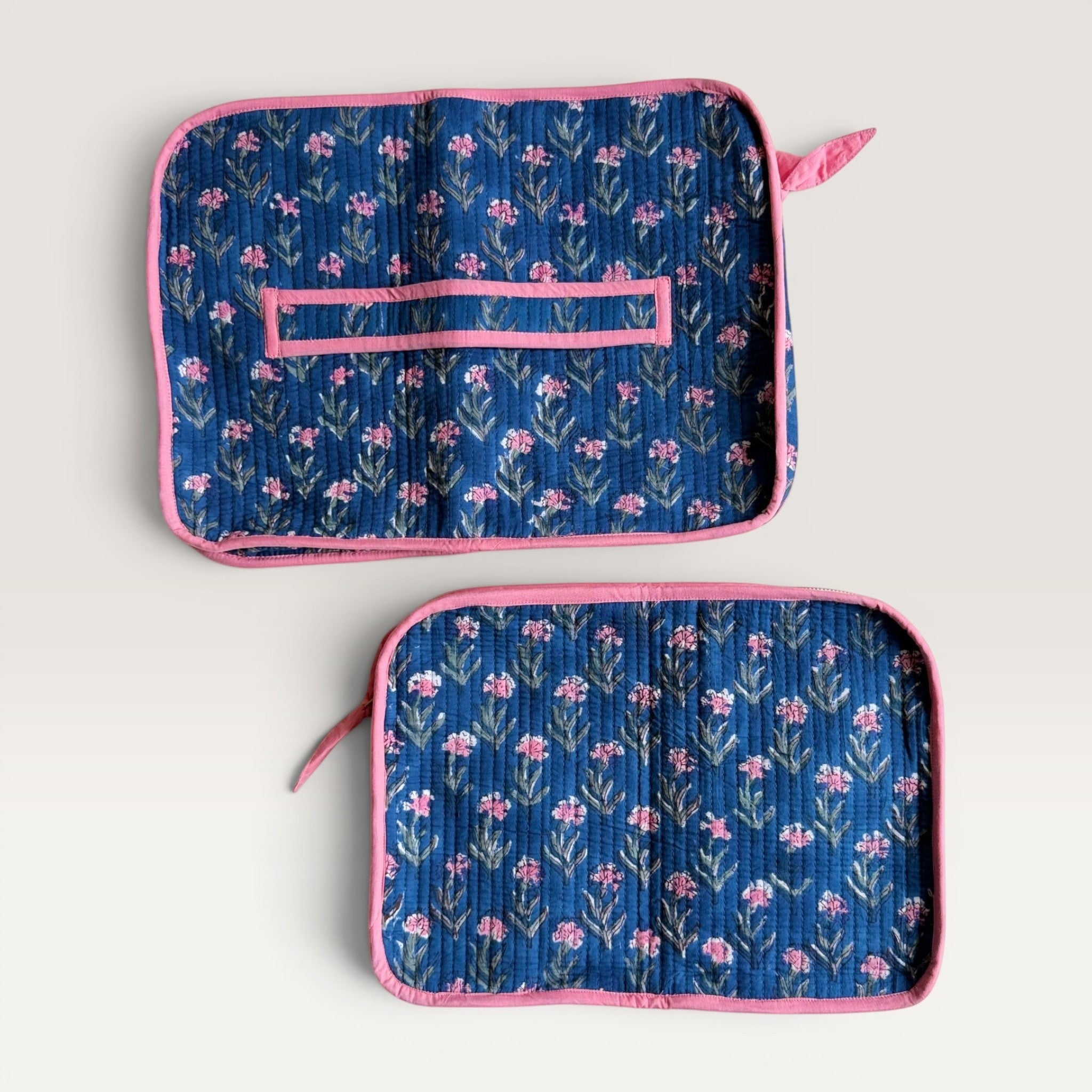 The Block & Bloom quilted navy blue laptop sleeve with pink carnation floral print, pink piping, and back hand strap.