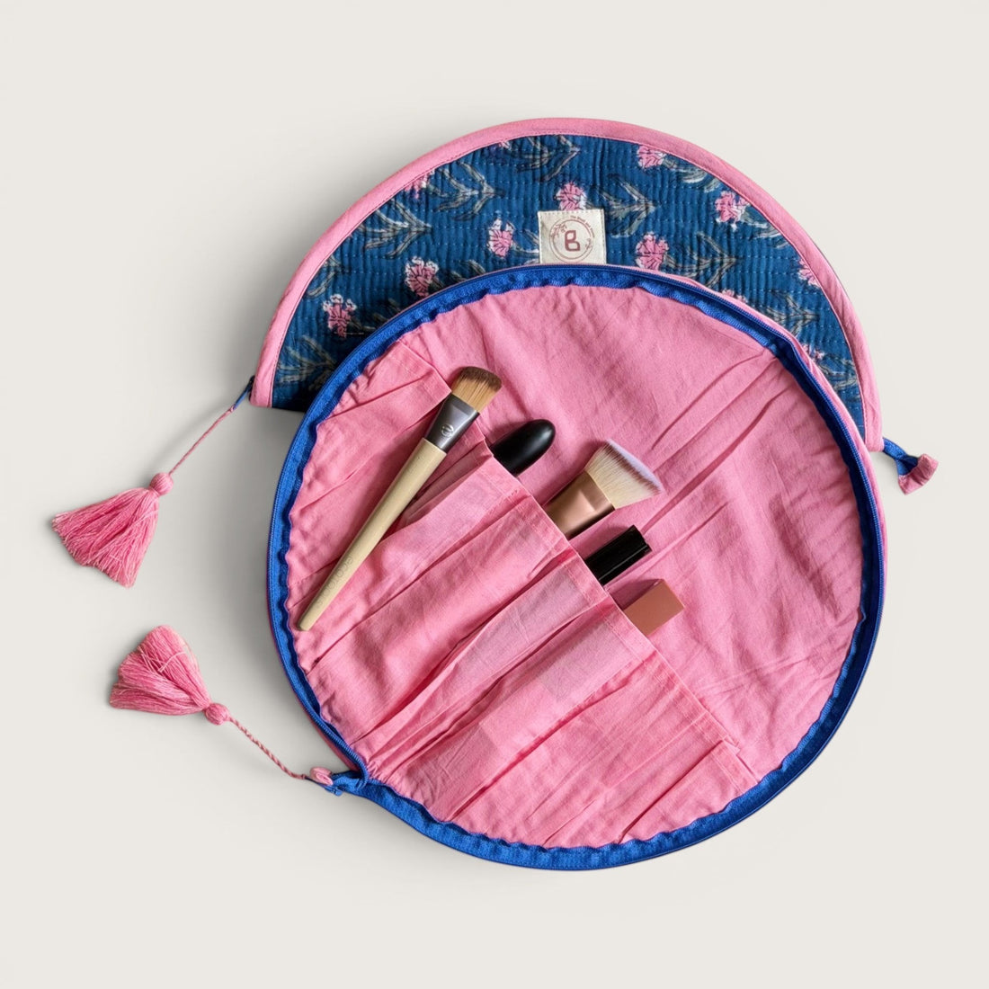 The Block & Bloom quilted makeup brush pouch in navy blue with pink carnation floral print and pink tassel zippers.