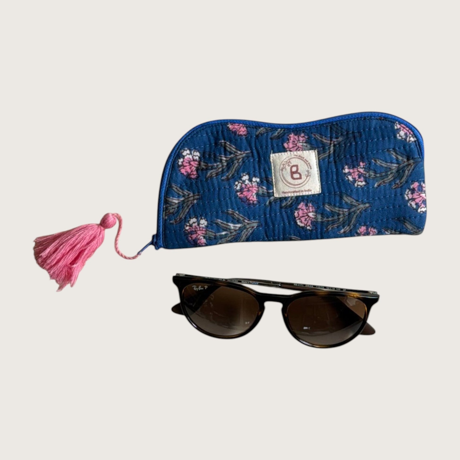 The Block & Bloom quilted cotton sunglasses pouch in navy with pink floral print and a pink tassel, shown with glasses
