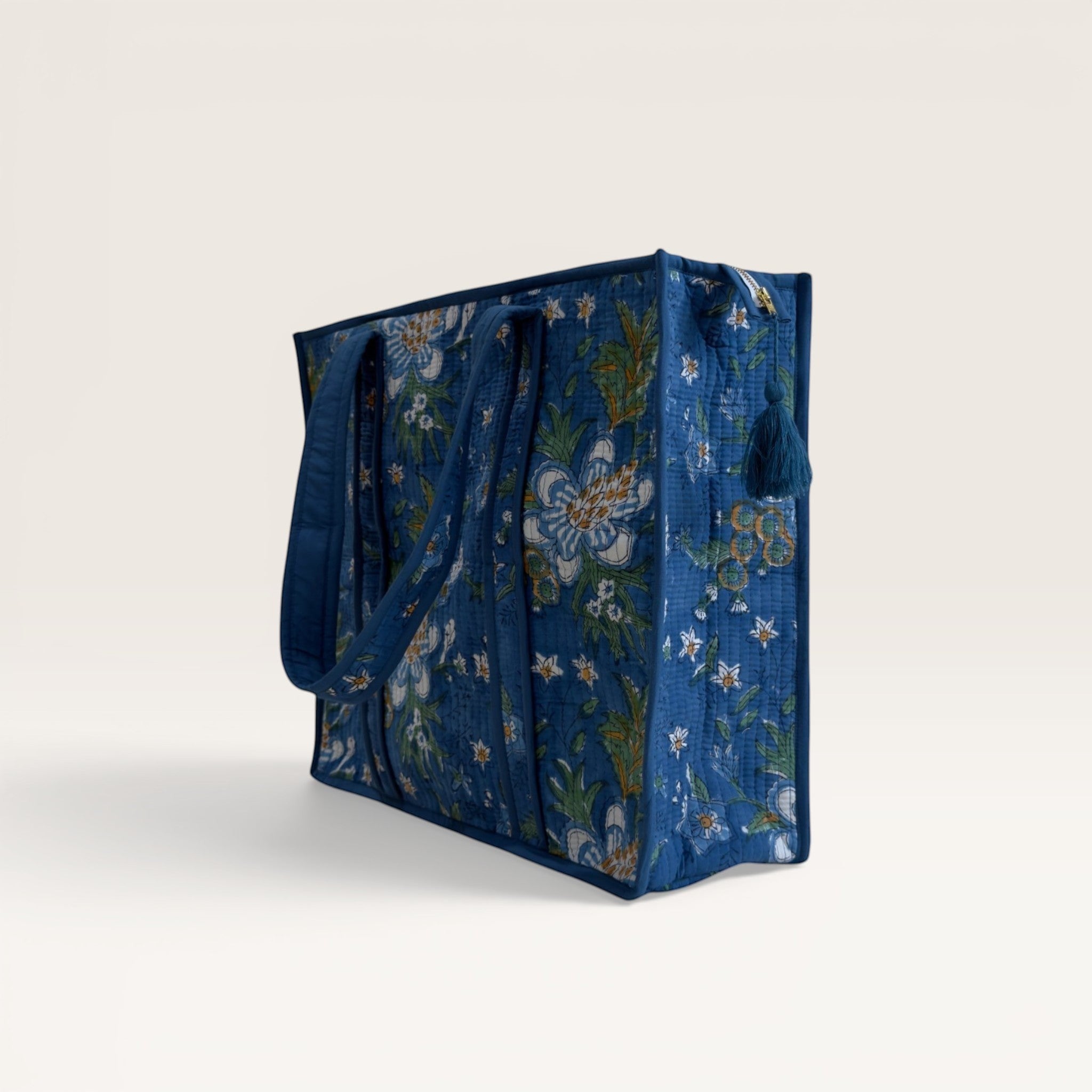 The Block & Bloom quilted tote bag in cobalt blue with white gardenia floral print and tassel zipper detail.