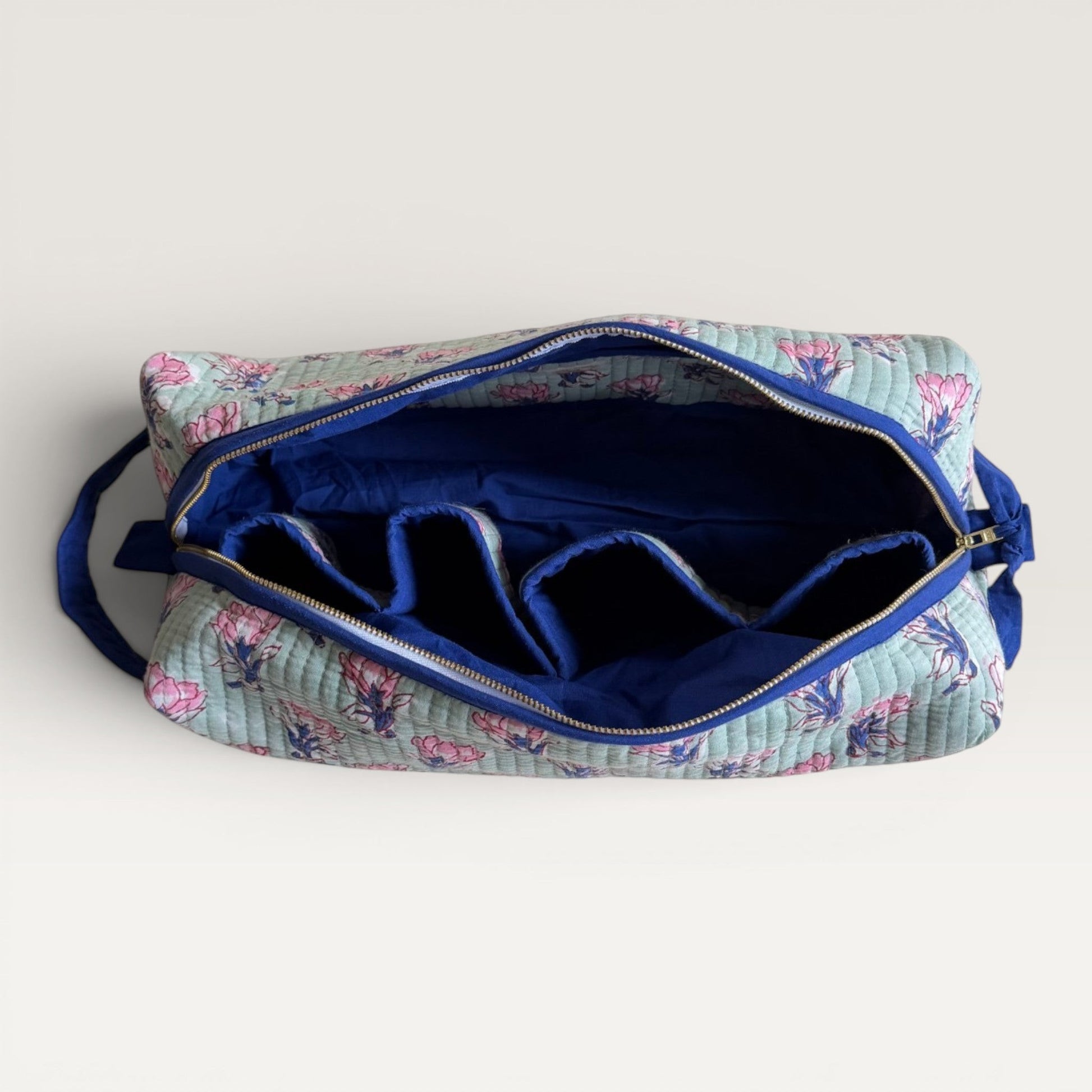 The Block & Bloom Saffron Sage quilted hair tool organizer bag with pink floral print, navy interior, and four slots.