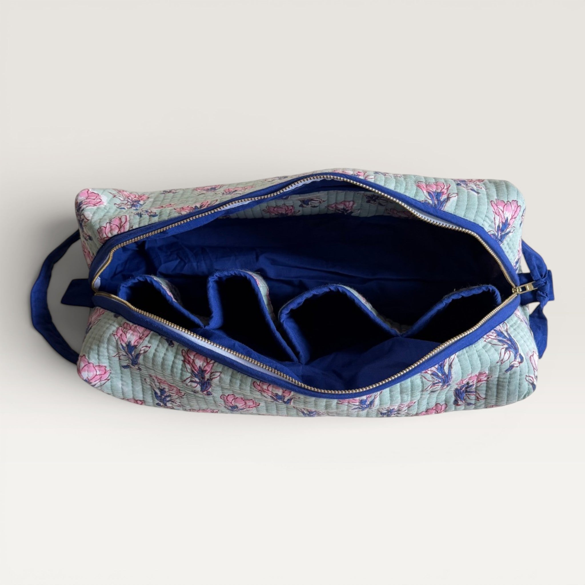 The Block & Bloom Saffron Sage quilted hair tool organizer bag with pink floral print, navy interior, and four slots.