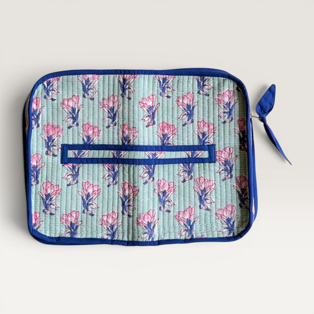 The Block & Bloom quilted laptop sleeve in sage green with pink saffron flower print and navy blue trim.