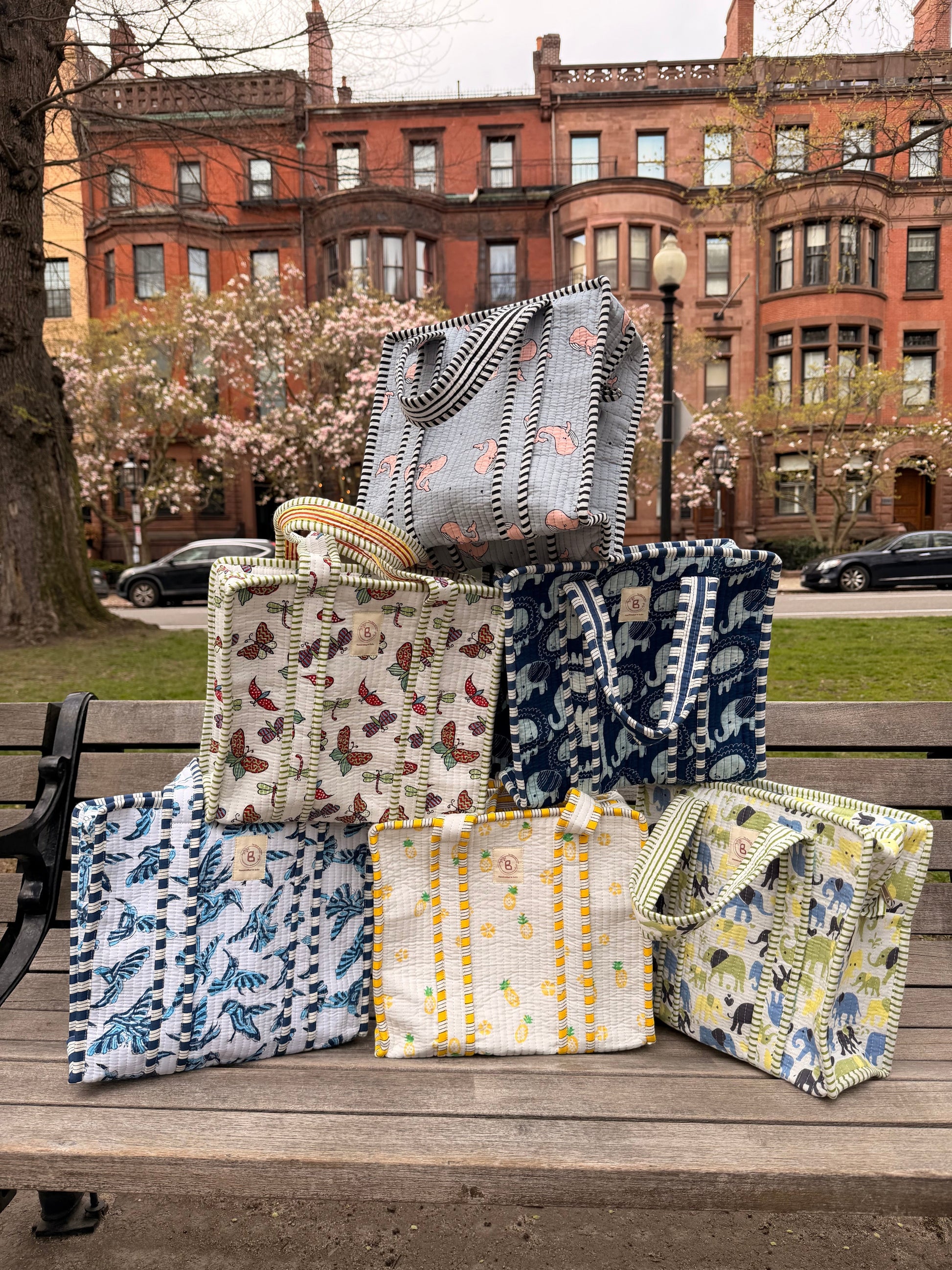 The Block & Bloom collection of quilted mini tote bags with colorful hand block-printed patterns stacked on a bench.