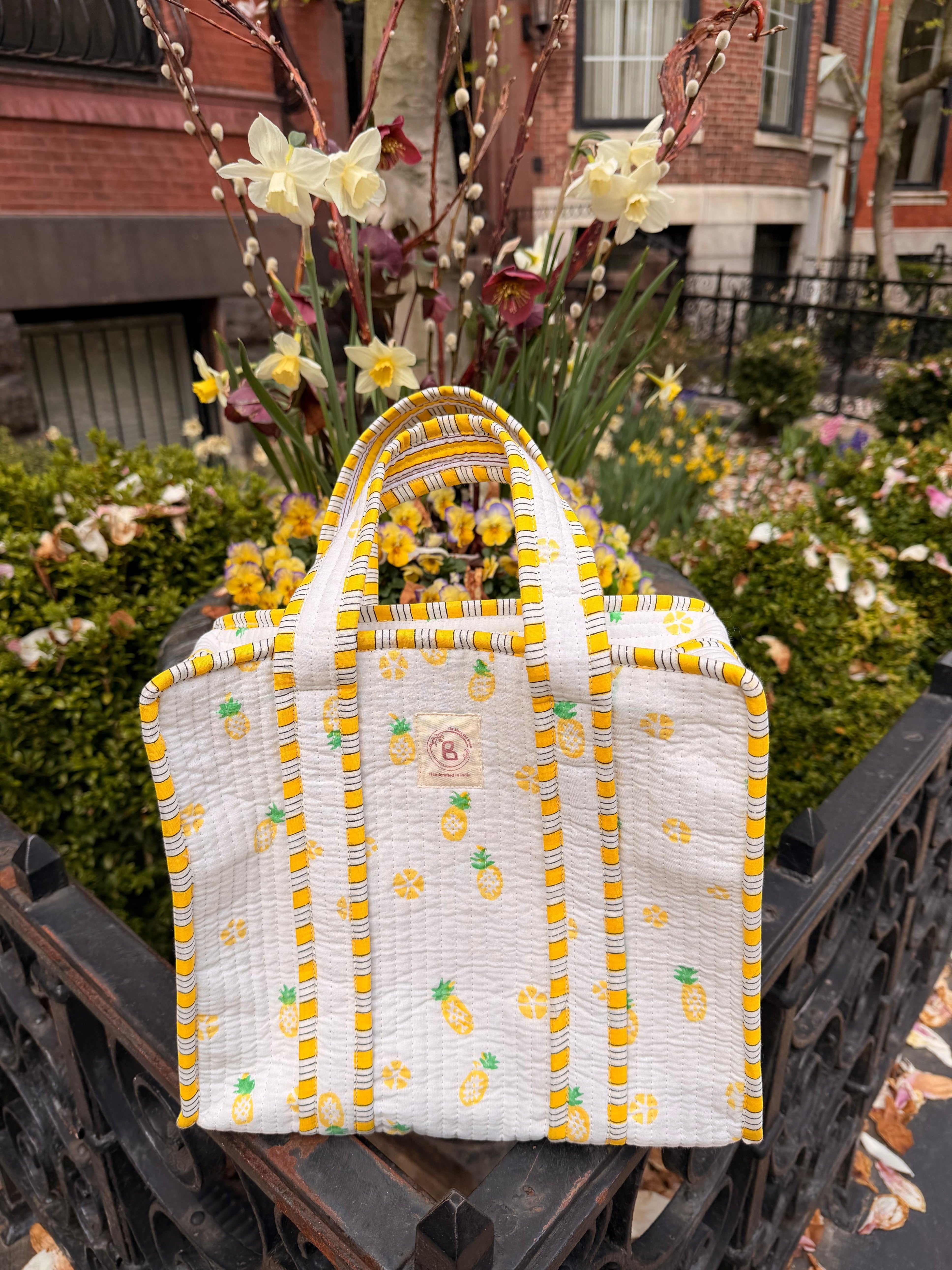 The Block & Bloom quilted mini tote with yellow pineapple print, white fabric, and yellow striped trim outdoors.