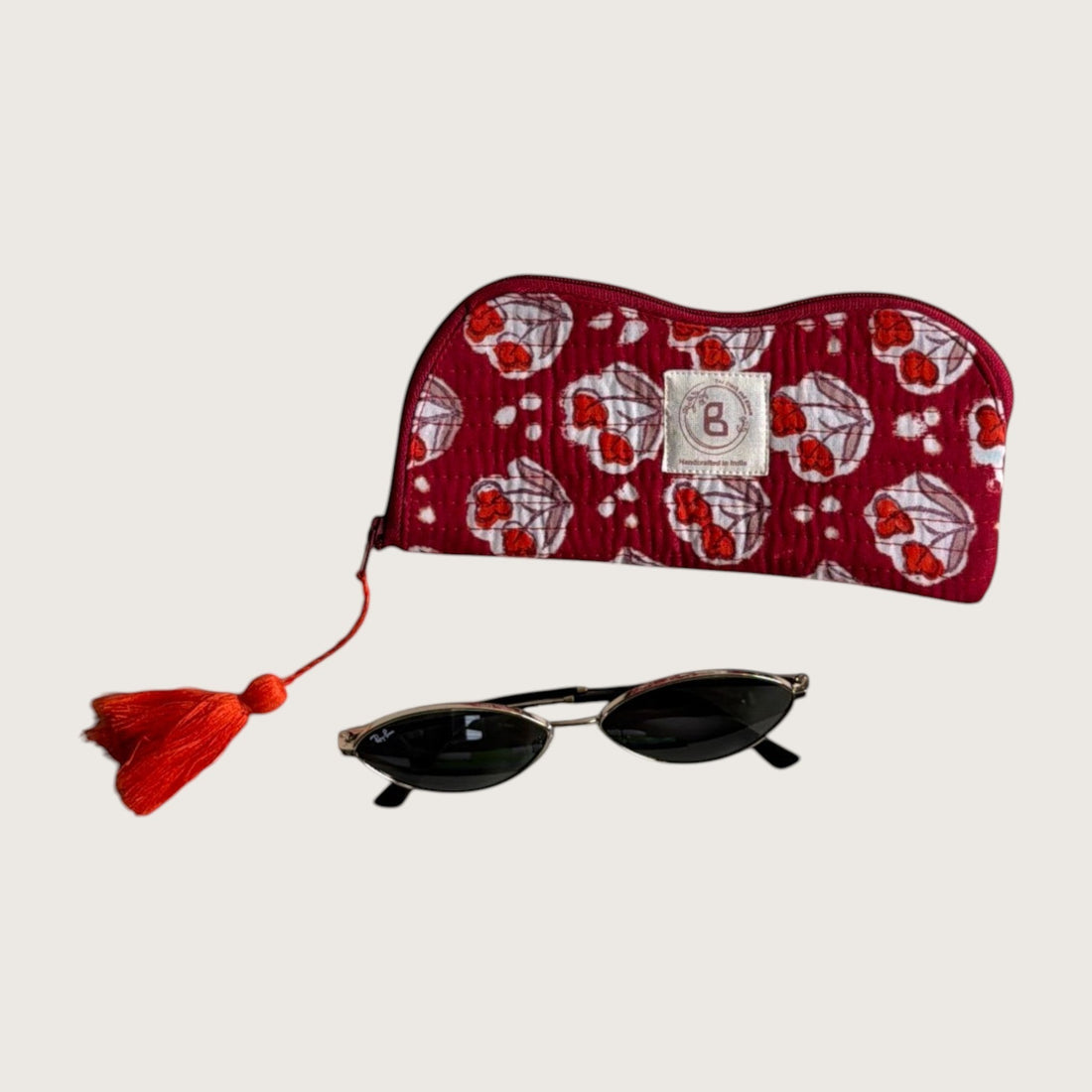 The Block & Bloom quilted sunglasses pouch in burgundy red with red tulip motifs, featuring a red tassel zipper pull.