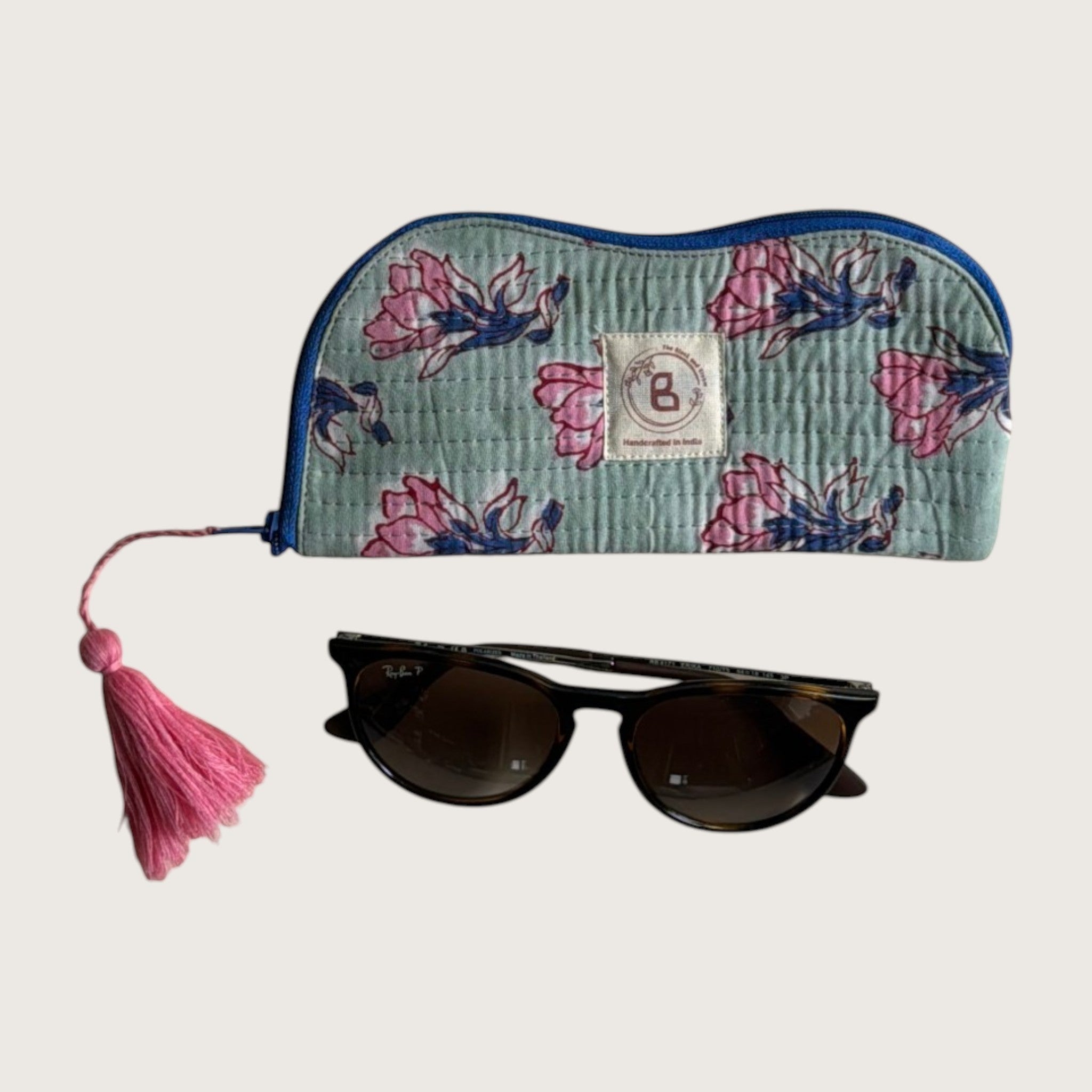 The Block & Bloom quilted cotton sunglasses pouch in sage green with pink floral print and a pink tassel zipper pull.