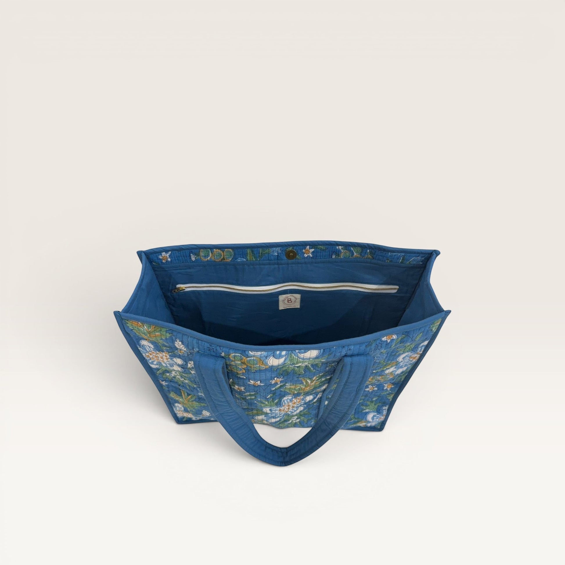The Block & Bloom Gardenia Bloom quilted tote bag in cobalt blue with white floral print, showing interior pockets.