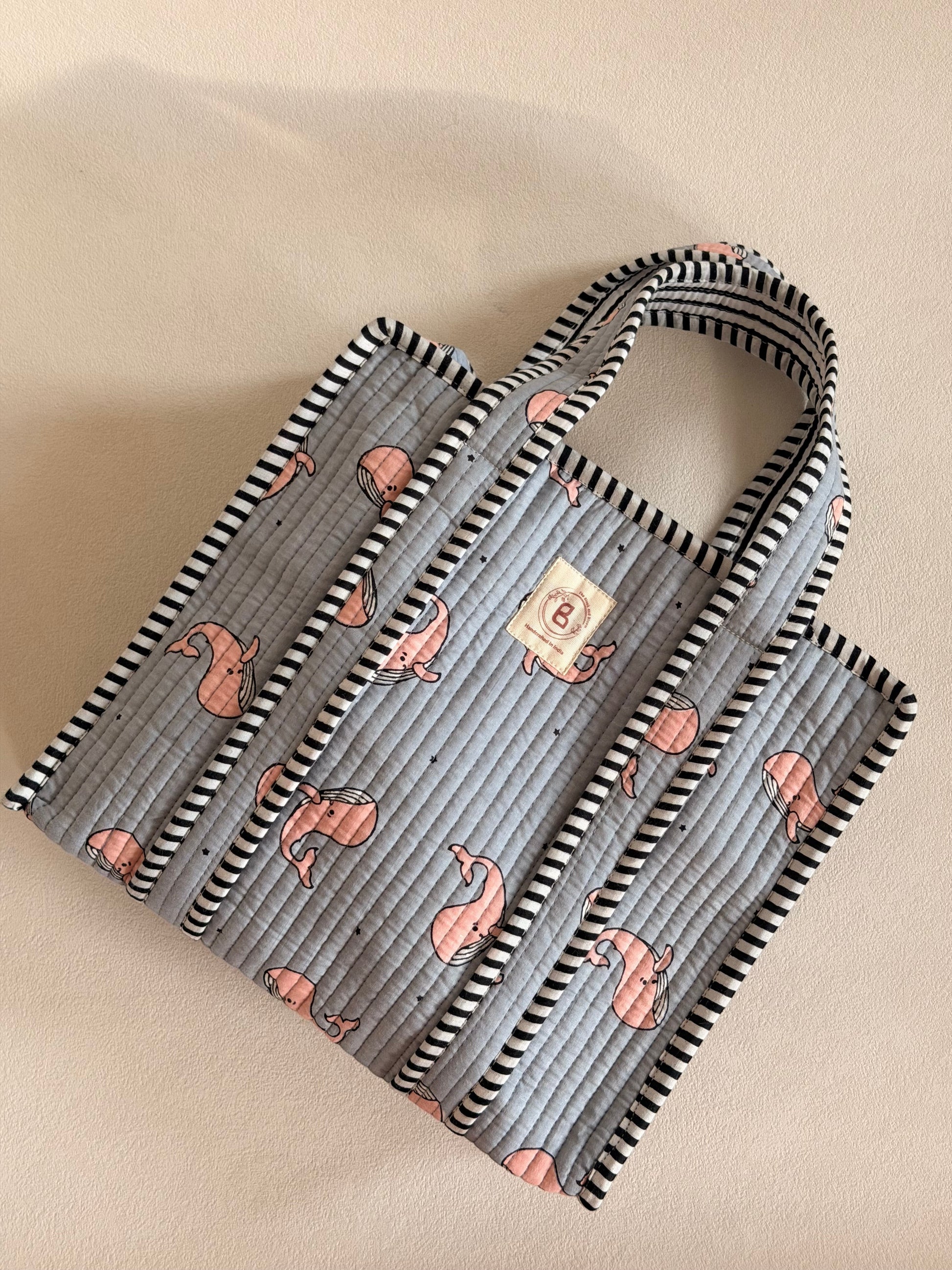 The Block & Bloom quilted mini tote in grey with pink whale print and black-and-white striped trim.