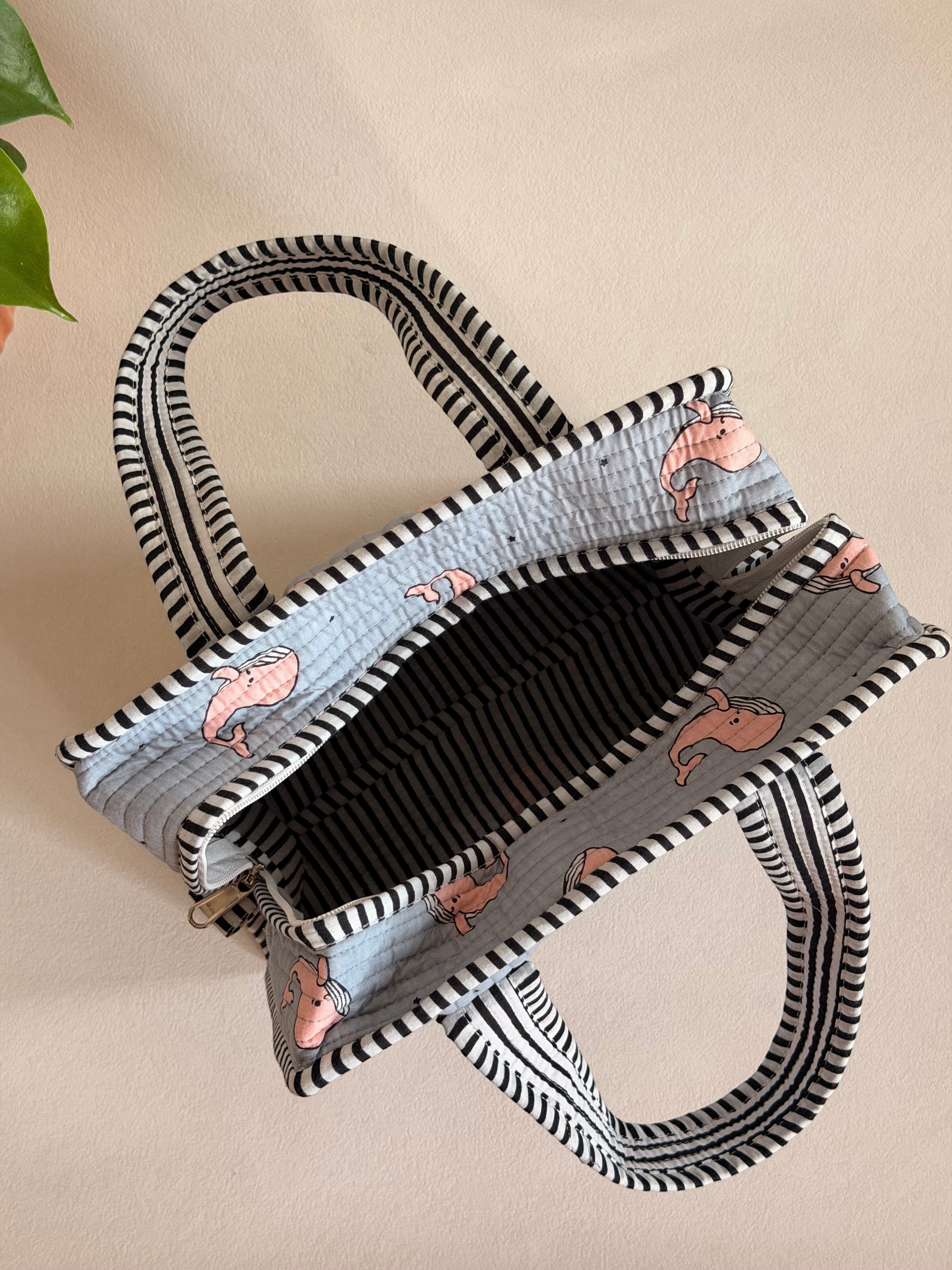 The Block & Bloom quilted mini tote in grey with pink whale print and black-and-white striped trim and handles.